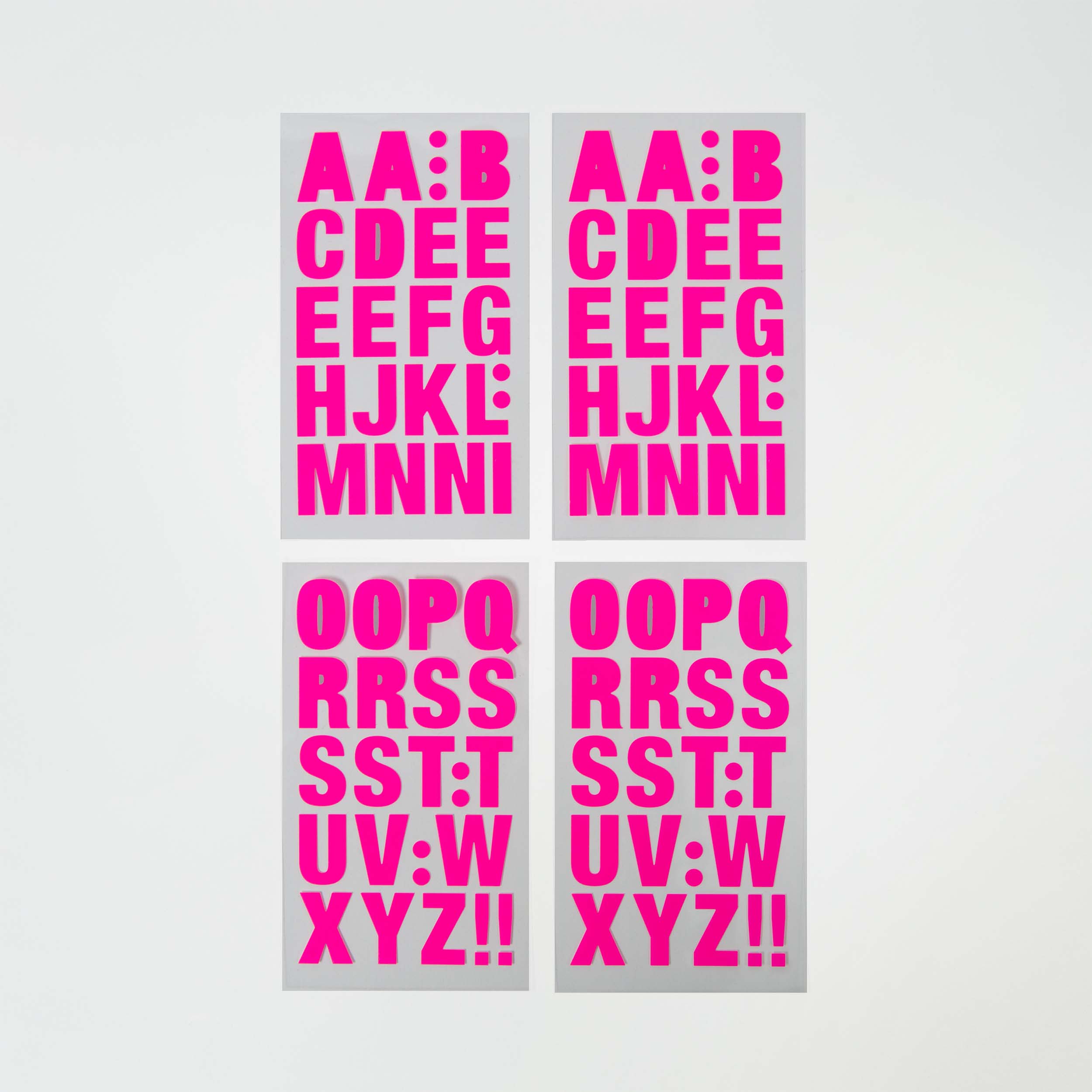 Vier in einem Raster angeordnete „Selbstklebende Buchstaben“-Poster von Paper Poetry zeigen kräftige, rosa Buchstaben auf weißem Hintergrund, jeweils in einer anderen Farbvariante von A bis Z.