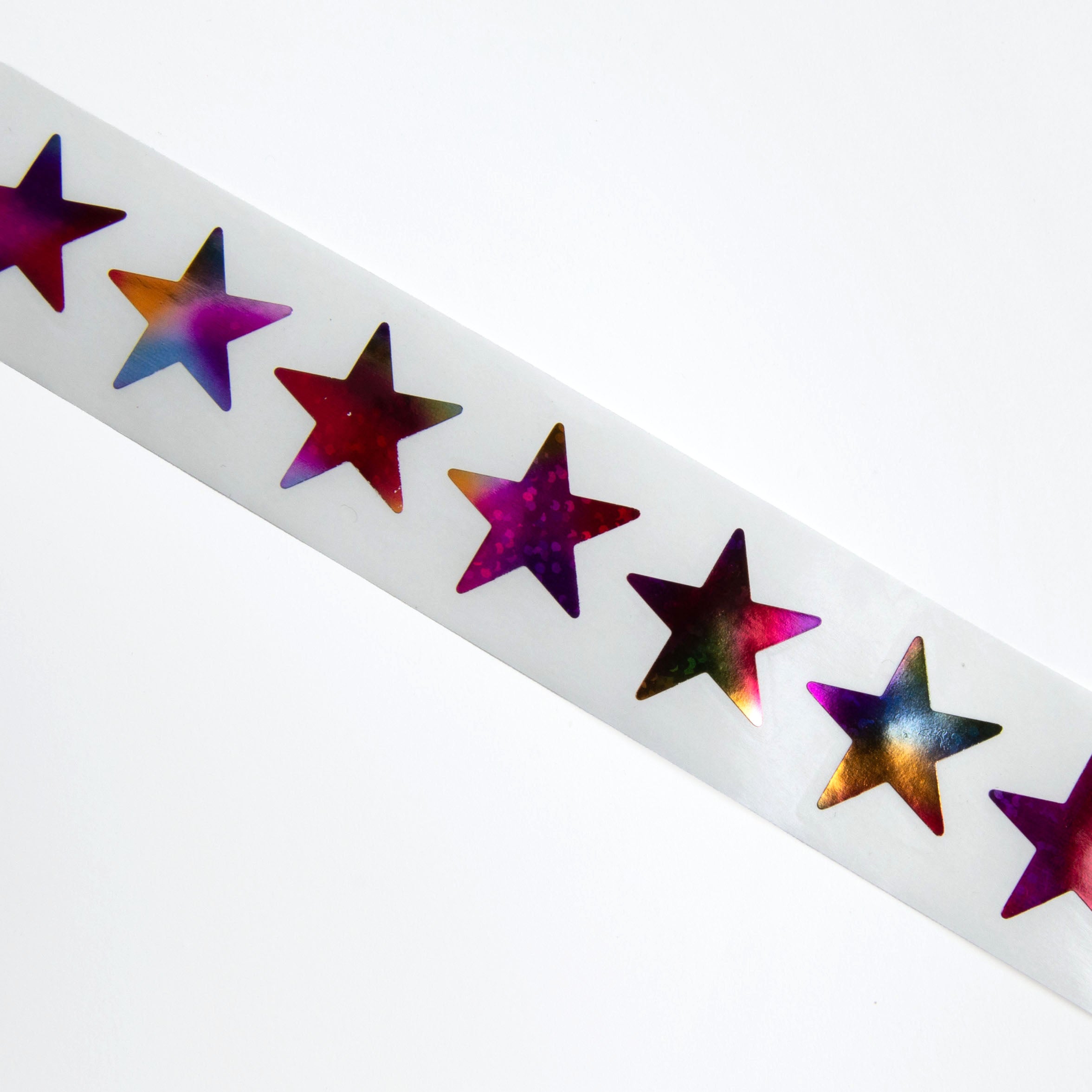 Ein weißer Streifen der Paper Poetry Mini-Sticker Sterne Rainbow von Paper Poetry zeigt leuchtende violette, rosa, goldene und blaue Sternchen, die in einer Reihe auf einem strahlend weißen Hintergrund angeordnet sind.