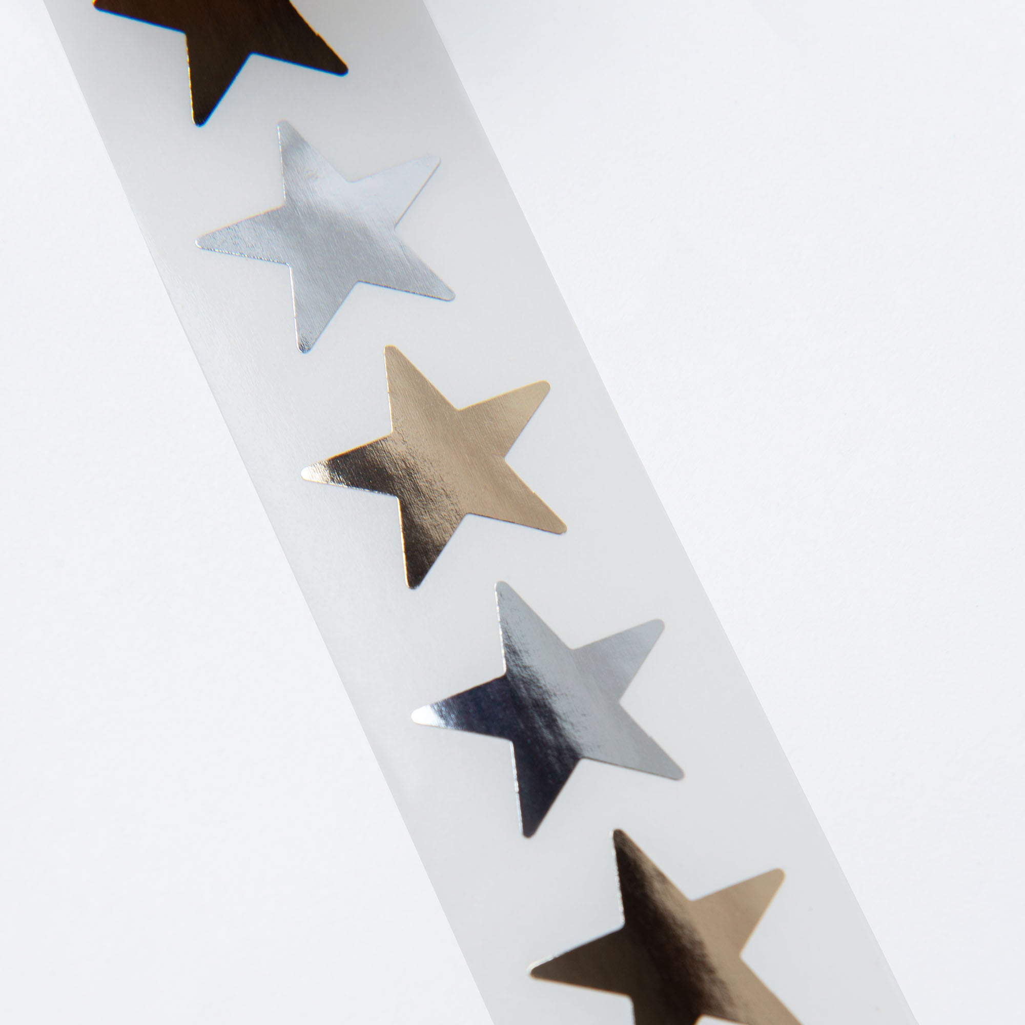 Ein Streifen reflektierender „Sterne“-Aufkleber von Paper Poetry zeigt abwechselnd silberne und goldene Sterne auf weißem Hintergrund und eignet sich ideal, um einen festlichen Weihnachtszauber zu verbreiten.