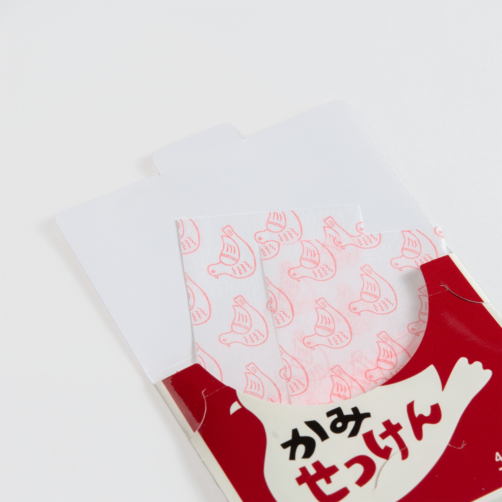 Eine Nahaufnahme einer teilweise geöffneten Hightide-Papierseifen-Verpackung zeigt dünne, weiße Blätter mit rosa Vogelmustern. Das japanische Retro-Design zeigt einen weißen Vogel auf rotem Grund - ideal für unterwegs.