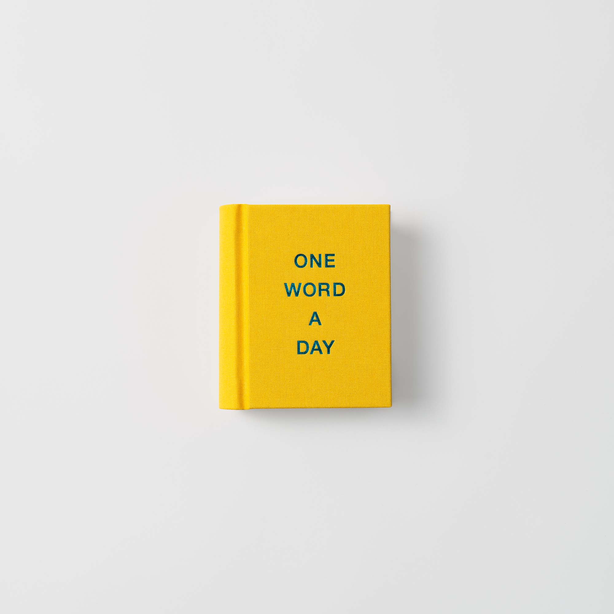 Ein kleines, handgefertigtes, gelbes OWAD-Klassiker-Mini-Notizbuch von paperlux mit ONE WORD A DAY in Blau auf dem Einband, zentriert auf Weiß - perfekt als einzigartige Geschenkidee.