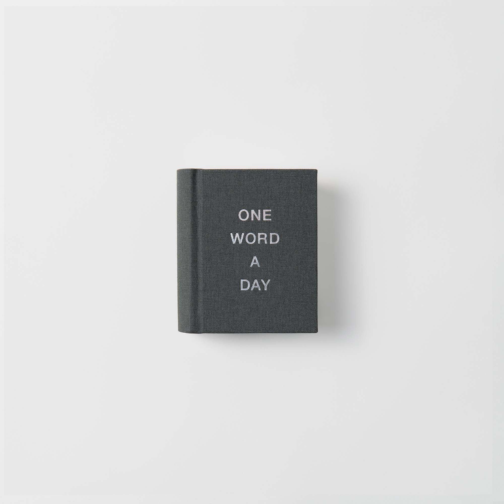 Der OWAD Klassiker von paperlux ist ein dunkelgraues Mini-Notizbuch mit "ONE WORD A DAY" in weißen Großbuchstaben auf einem Leineneinband, zentriert auf weißem Hintergrund - perfekt als Geschenk.