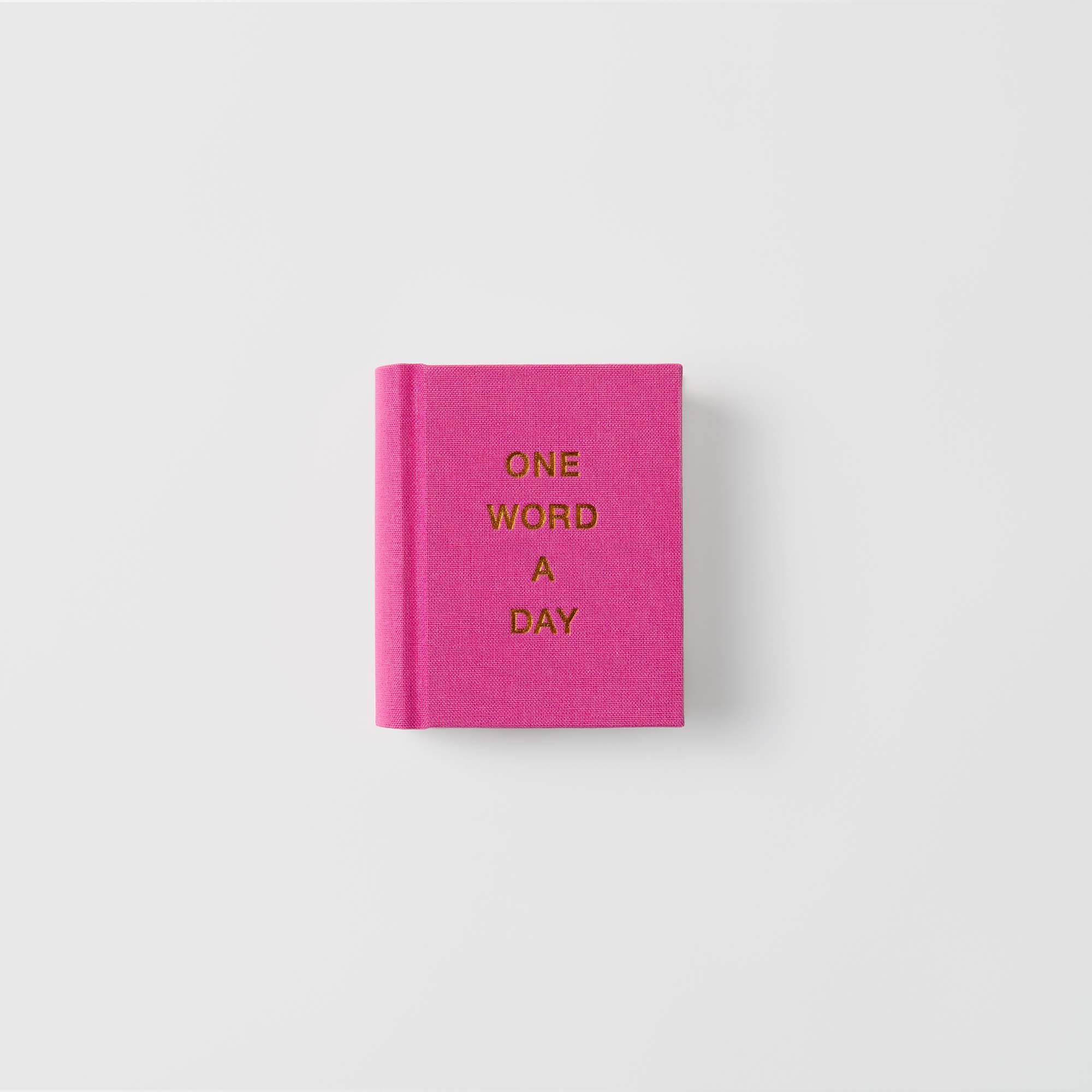 Ein leuchtend rosafarbenes OWAD-Klassiker-Mini-Notizbuch aus Papierlux mit der Aufschrift "ONE WORD A DAY" in Gold auf dem Leineneinband ist vor einem weißen Hintergrund abgebildet - ein perfektes Geschenk.