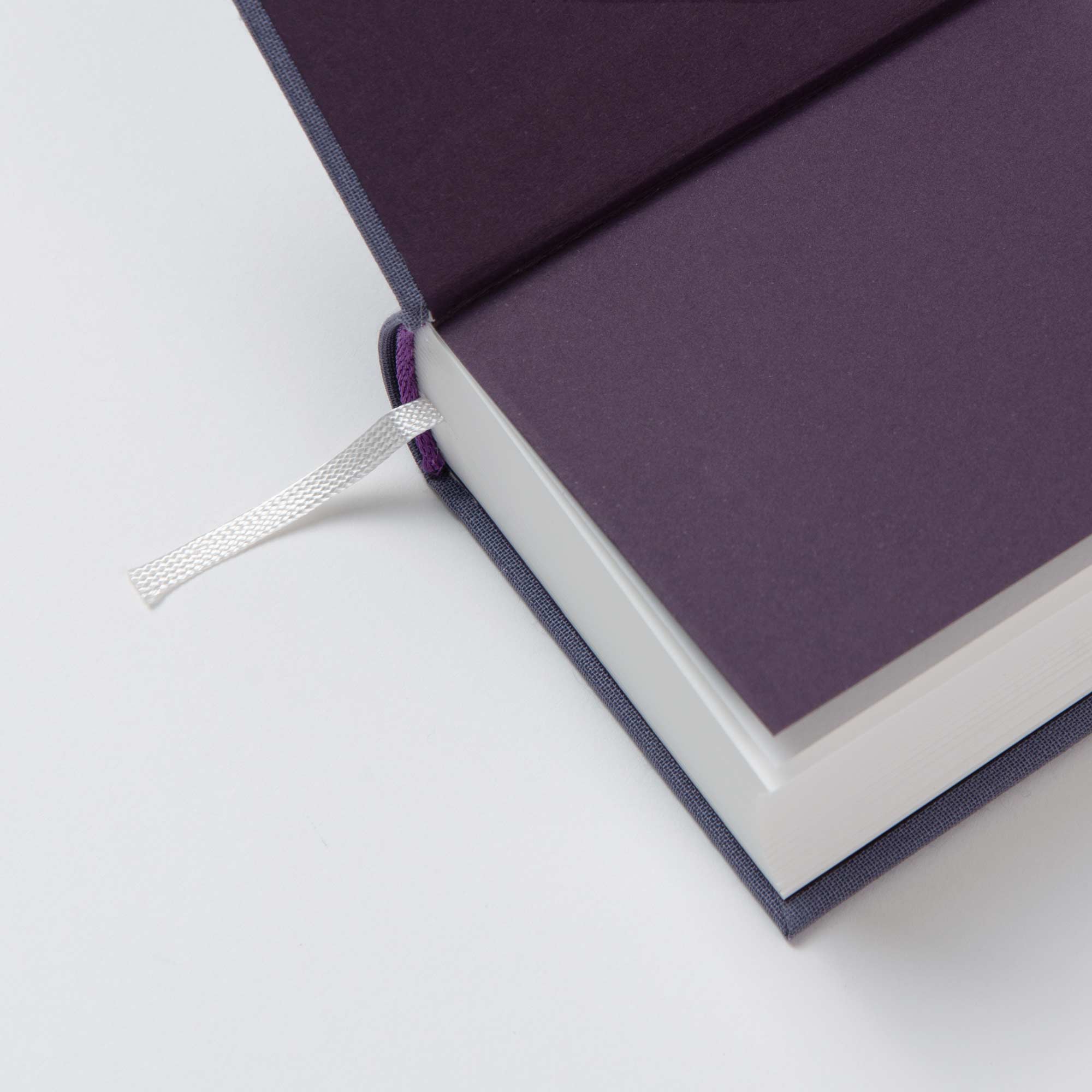 Das OWAD Elements von paperlux - ein handgefertigtes Hardcover-Buch mit dunkelviolettem Vorsatzpapier und weißem Lesezeichen - ist ein einzigartiges Geschenk und ruht elegant auf einer weißen Oberfläche.
