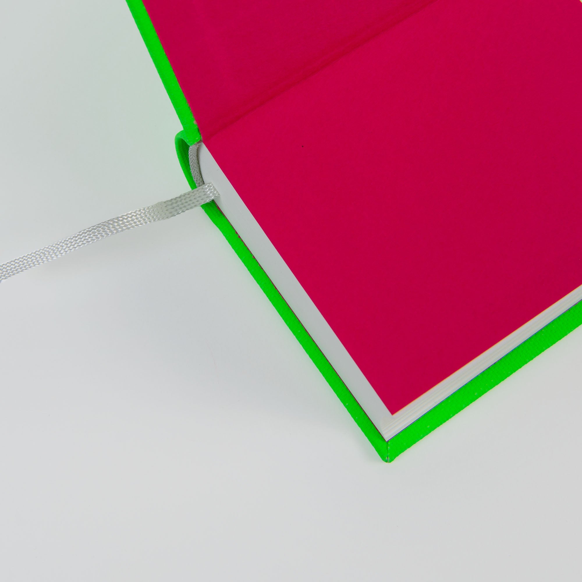 Das OWAD Neon-Notizbuch von paperlux hat einen leuchtend grünen Einband mit pinkfarbenen Innenseiten, schräg von oben gesehen. Es eignet sich perfekt für Tagebucheinträge oder als Geschenkidee und enthält ein weißes Lesezeichen mit Band auf einem sauberen weißen Hintergrund.