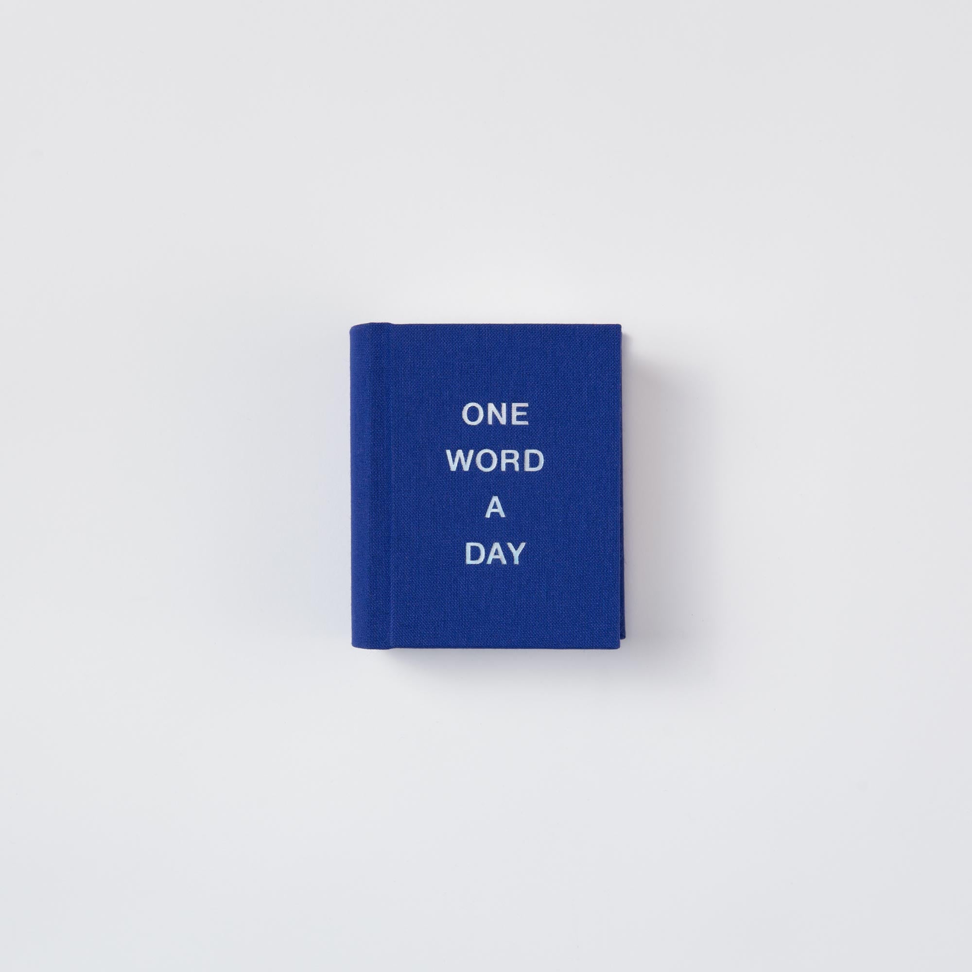Ein kompaktes blaues OWAD Shine Bright Mini-Notizbuch von paperlux mit "ONE WORD A DAY" in weißen Großbuchstaben auf dem Einband. Ideal als Geschenk, wird das Notizbuch zentriert vor einem schlichten weißen Hintergrund präsentiert.