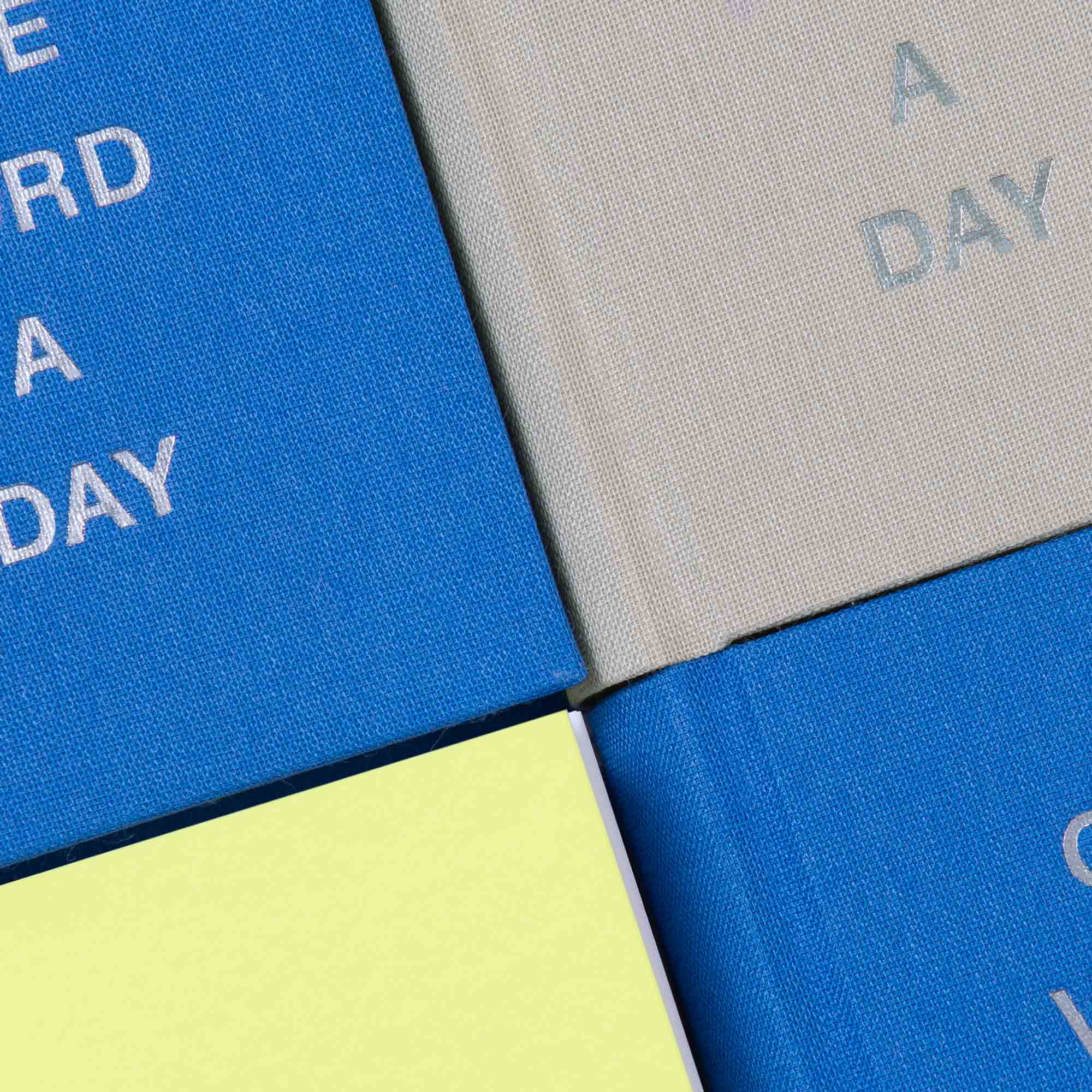 Vier gebundene Paperlux OWAD Urban-Bücher sind in einem Raster angeordnet. Drei Einbände sind blau und einer ist hellgrau und tragen jeweils den Text "A WORD A DAY". Das Buch unten links hat einen blassgelben Einband.