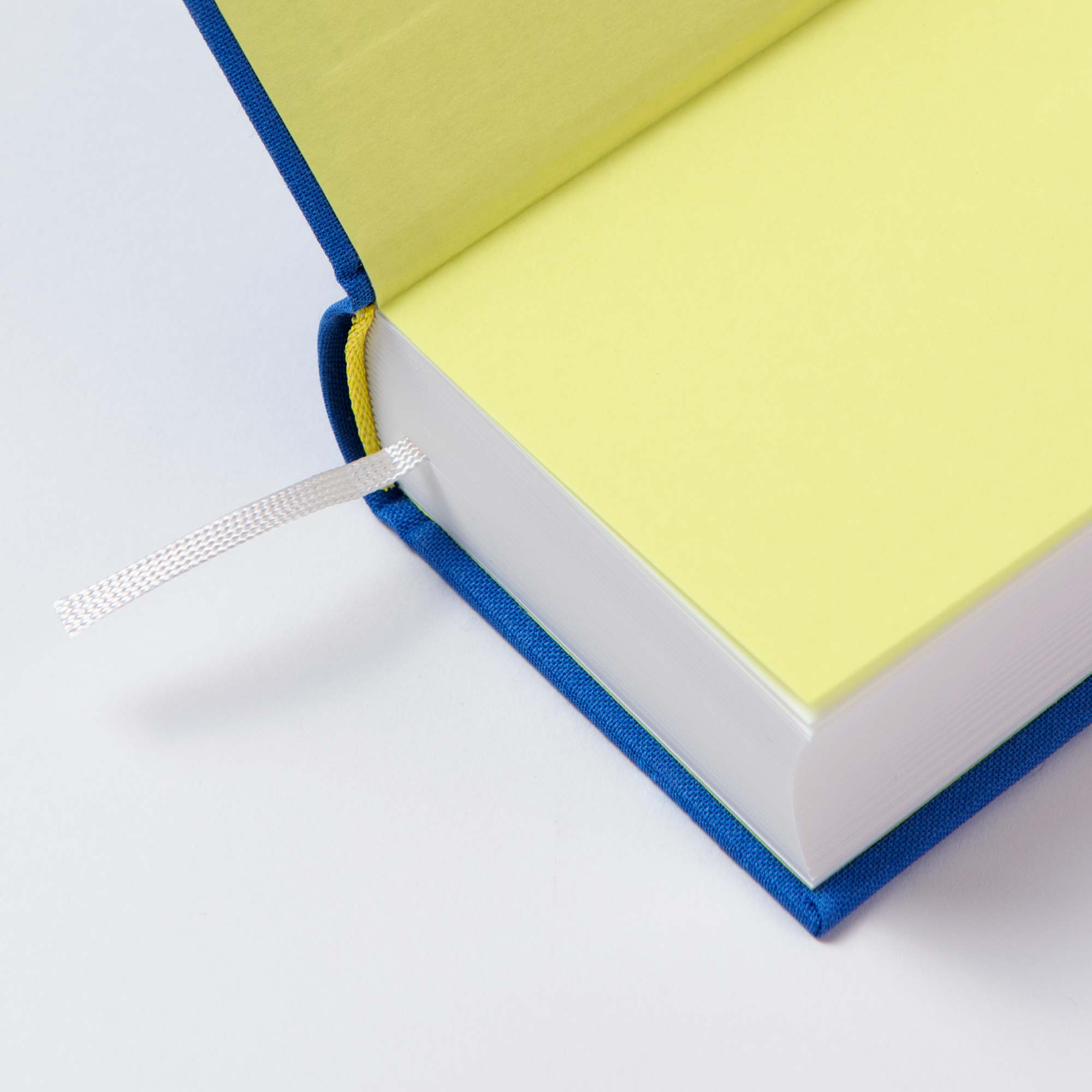 Nahaufnahme eines aufgeschlagenen Paperlux OWAD Urban mit gelben Seiten, einem blauen Leineneinband (Fadengeheftet) und einem weißen Lesezeichenband zwischen den Seiten.