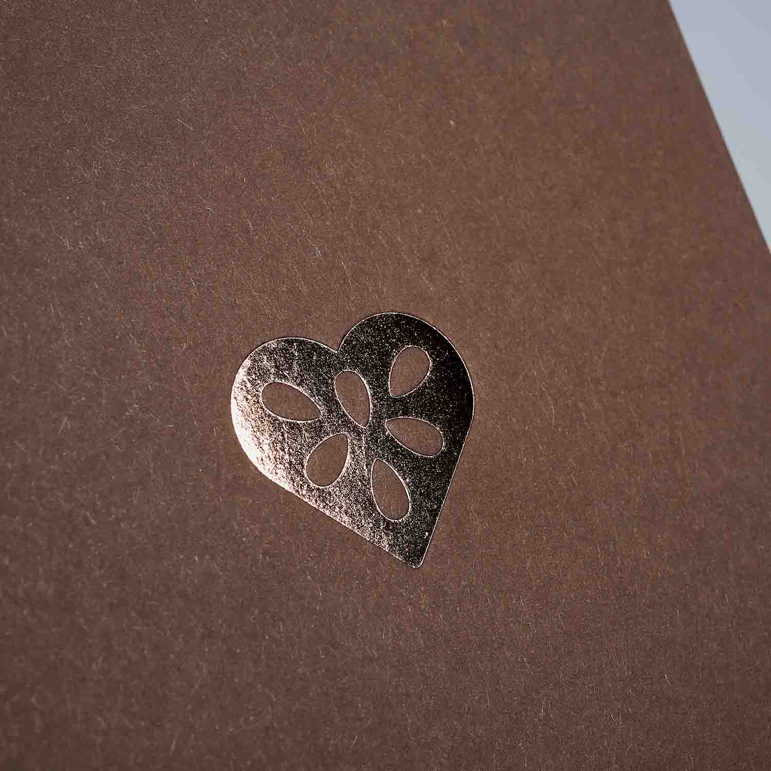 Ein Metallic-Herz mit Blütenausschnitten ist auf einer braunen, strukturierten Oberfläche aus dem paperlux.store Weihnachtskarten 3-er Set Madarine, Silver, Chocolate geprägt.