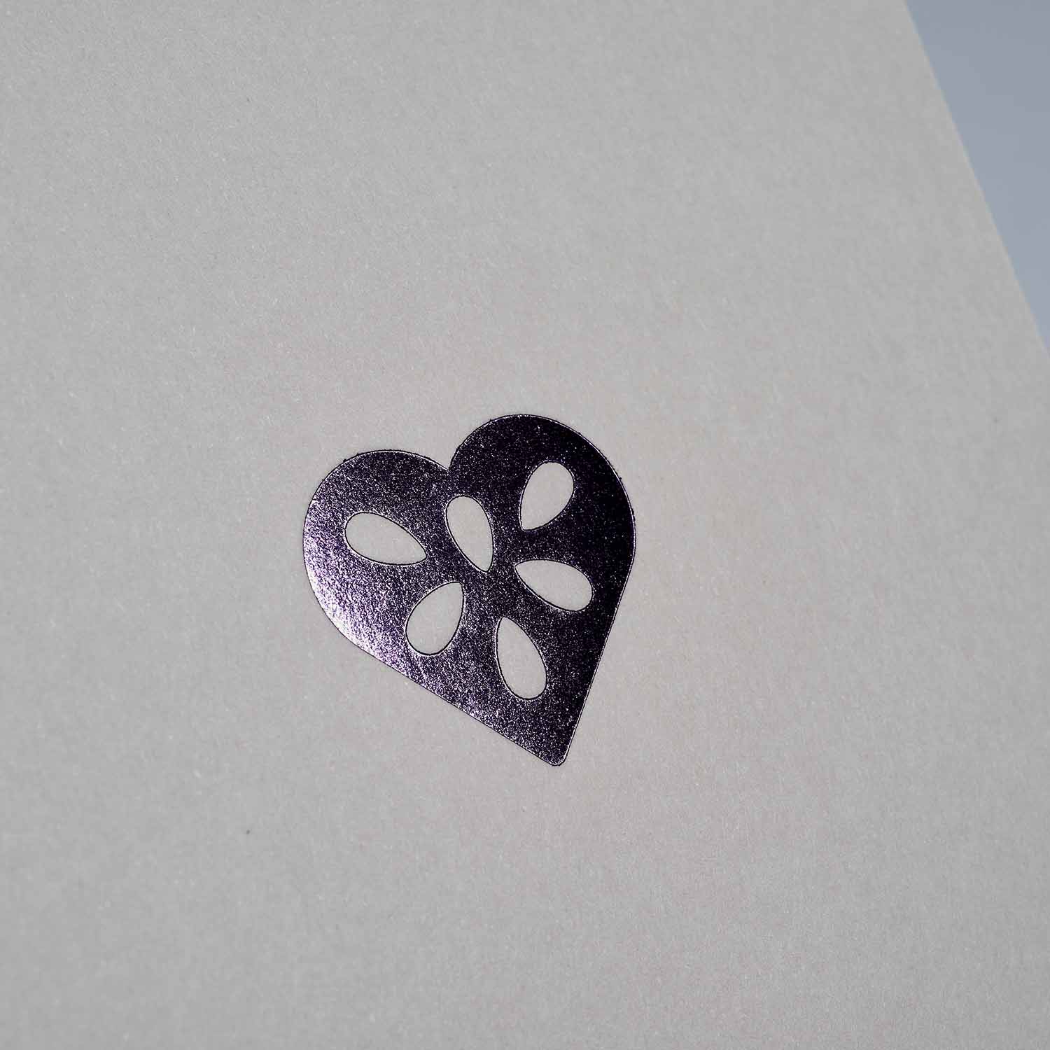 Ein silberfarbenes Metallic-Herz mit Tränenausschnitten ziert eine weiße Karte - ideal für das Weihnachtskarten 3-er Set Chocolate, Shadow, Silver Dust von paperlux.store oder um einer A6-Grußkarte Eleganz zu verleihen.