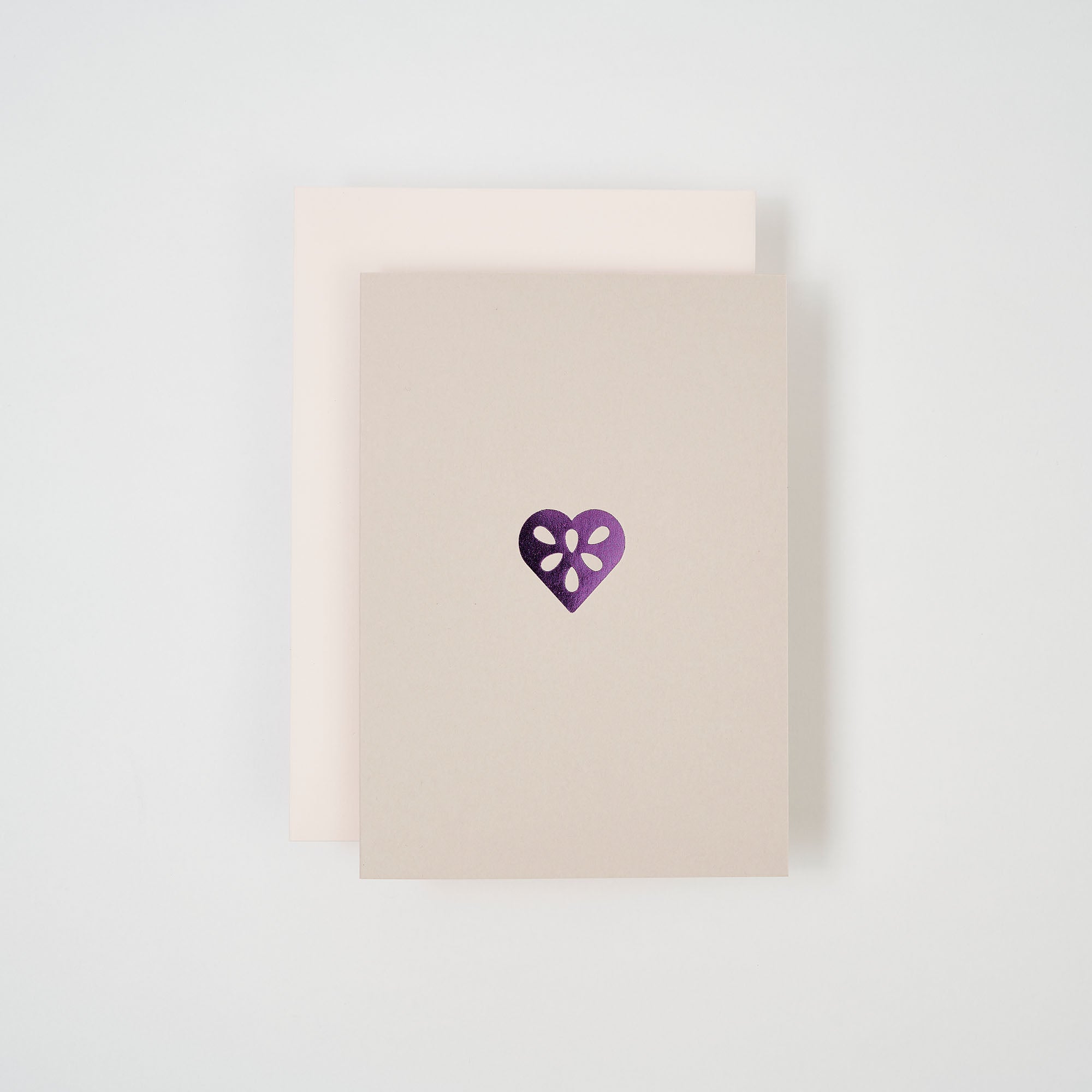 Zwei minimalistische Karten von paperlux.store sind auf einem weißen Hintergrund gestapelt. Die oberste, die Weihnachtskarte Lebkuchenherz, ist beige mit einem glänzenden lila Herz; darunter befindet sich eine hellcremefarbene Karte, leicht versetzt.