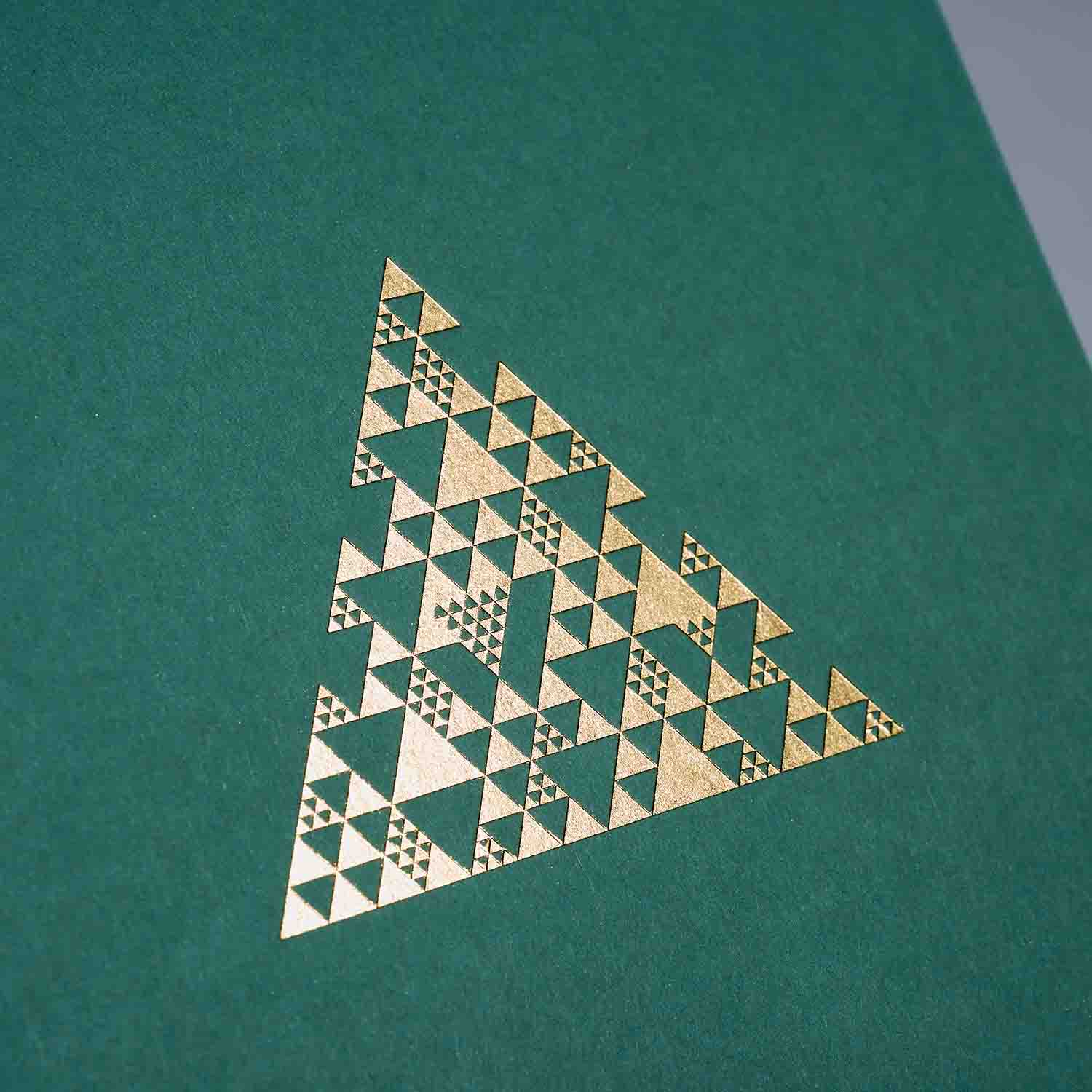 Ein goldenes Dreieck mit verschlungenen geometrischen Mustern auf grünem Hintergrund ziert das paperlux.store Weihnachtskarten 2er-Set Coral & Sage - ideal als einzigartige A6 Klappkarte.