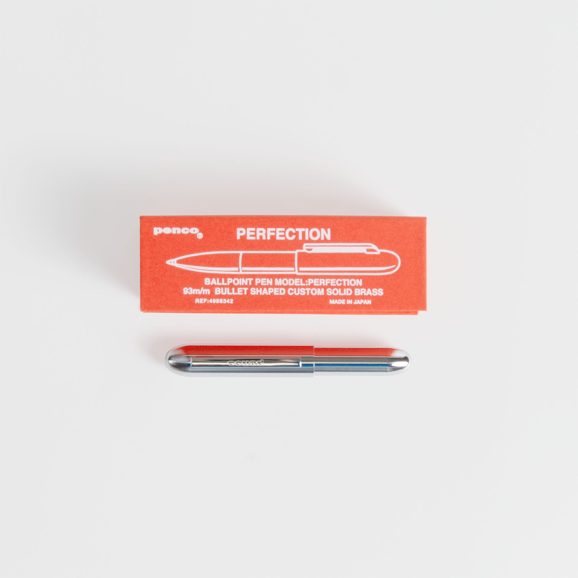 Eine rote PERFECTION Box mit einer Stift-Illustration sitzt über einem silbernen Kompakt-Kugelschreiber - Bullet Pen von paperlux.store (Messinggehäuse schwarz) auf weiß. CUSTOM SOLID BRASS und Hergestellt in Japan sind auf der Box hervorgehoben.