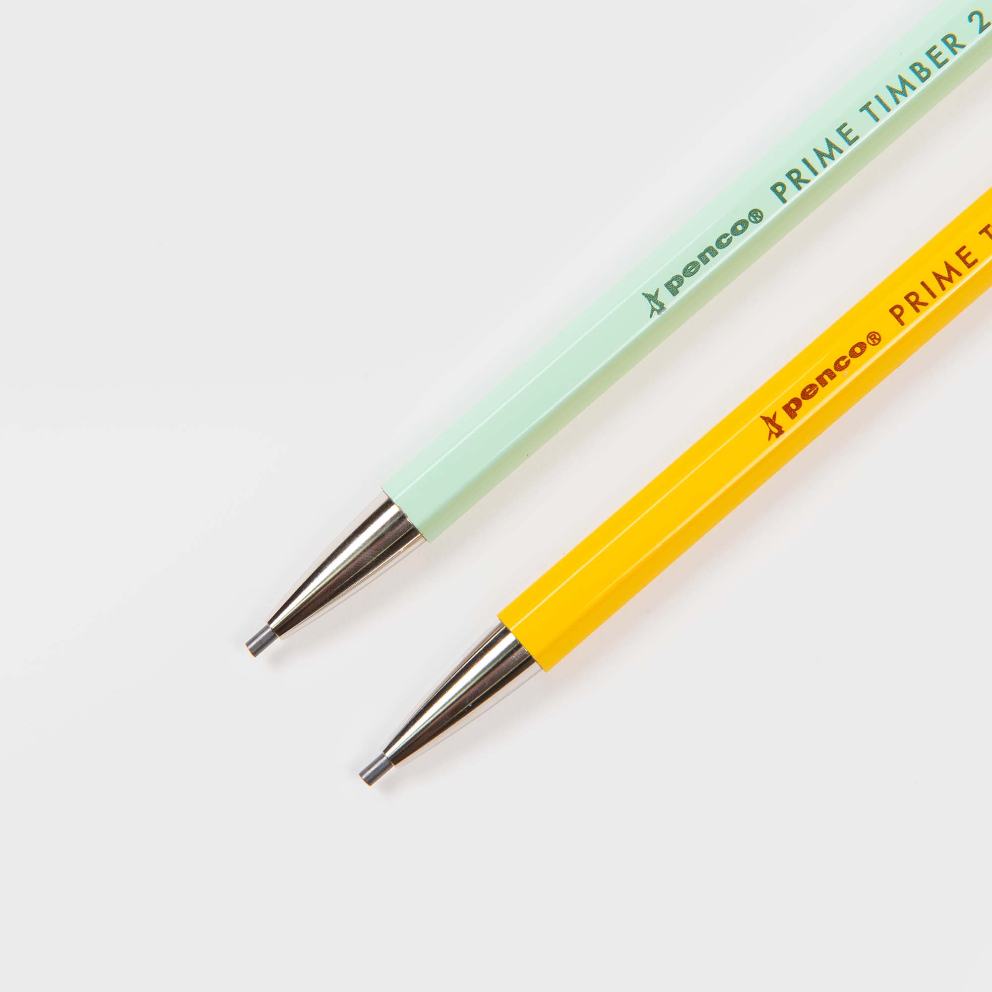 Zwei Penco Prime Timber Druckbleistifte mit 2 mm Minen und Metallspitzen, einer in hellgrün und einer in gelb, liegen diagonal auf einem weißen Hintergrund. Beide zeigen japanisches Design mit dem Schriftzug "Prime Timber" in der Nähe des oberen Randes.