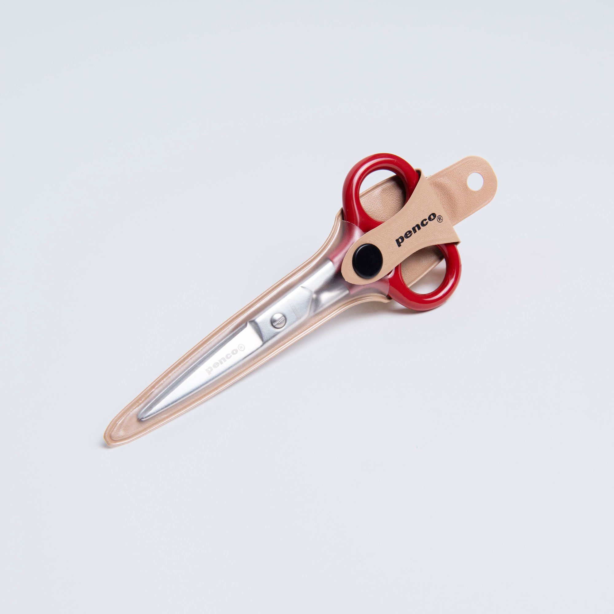 Die Edelstahl Schere - S von Penco verfügt über eine Schere mit rotem Griff in einer beigen Lederhülle mit geprägtem Markennamen und einem Griff mit Knopfverschluss, alles vor einem schlichten weißen Hintergrund.