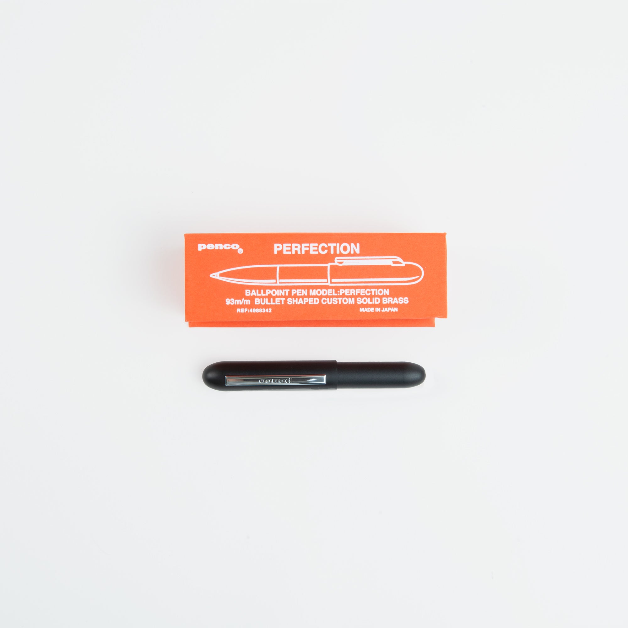Ein schwarzer Kompakt-Kugelschreiber - Bullet Pen von paperlux.store ruht unter einer orangefarbenen PERFECTION-Box mit weißem Text und einer Stift-Illustration, alles vor einem schlichten weißen Hintergrund. Hergestellt in Japan.