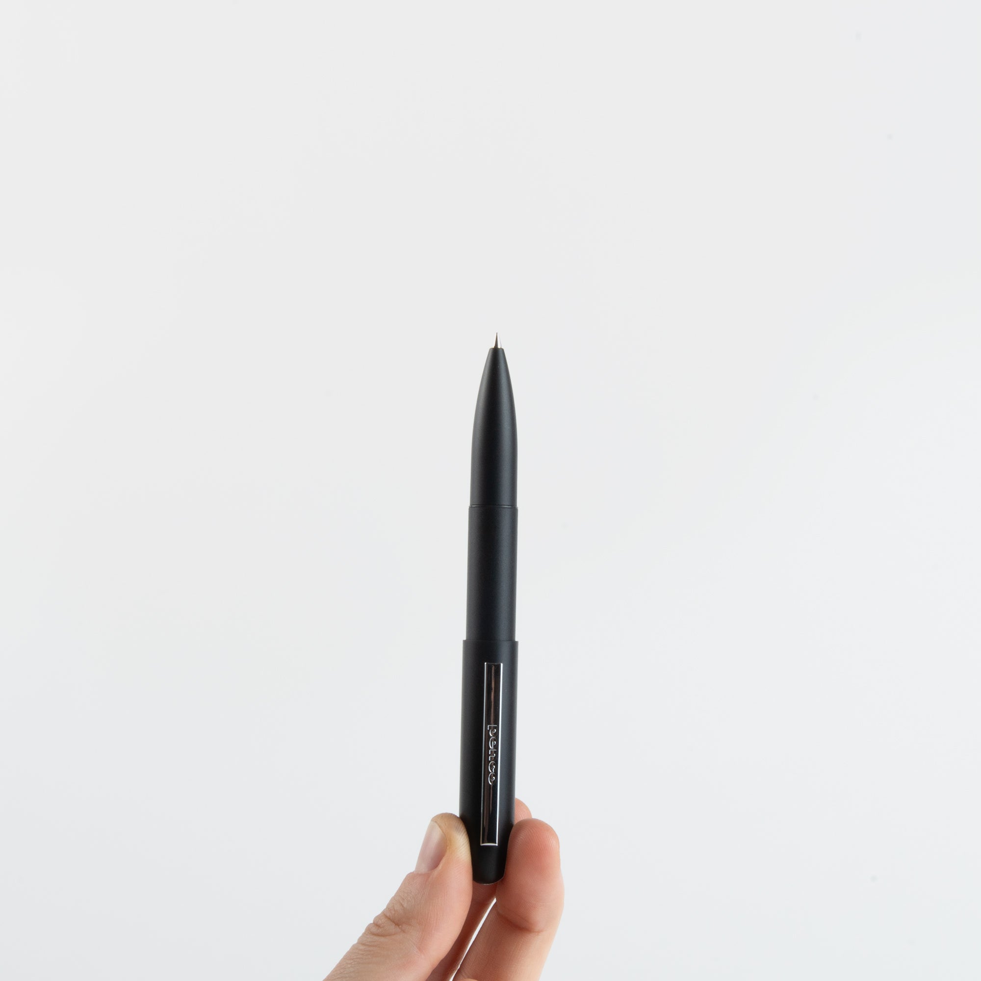 Eine Hand hält einen Kompakt-Kugelschreiber - Bullet Pen schwarz von paperlux.store aufrecht vor einem schlichten weißen Hintergrund, made in Japan.