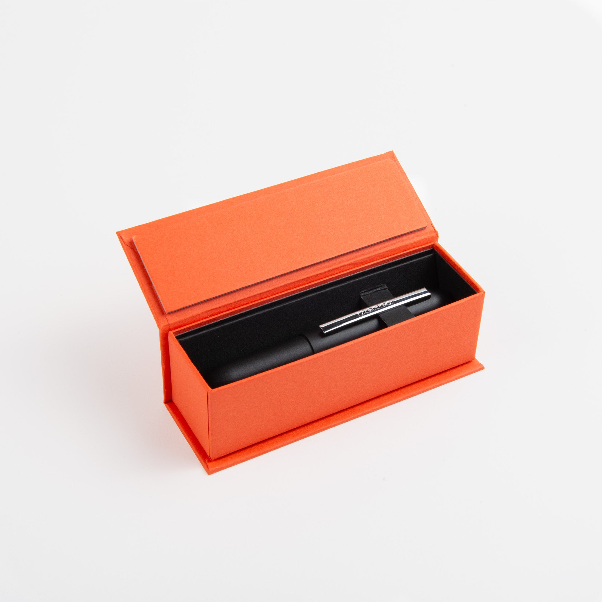 Der Kompakt-Kugelschreiber - Bullet Pen schwarz von paperlux.store, mit silbernem Clip und Messinggehäuse, wird in einer offenen, rechteckigen orangefarbenen Box auf weißem Hintergrund gezeigt. Hergestellt in Japan.