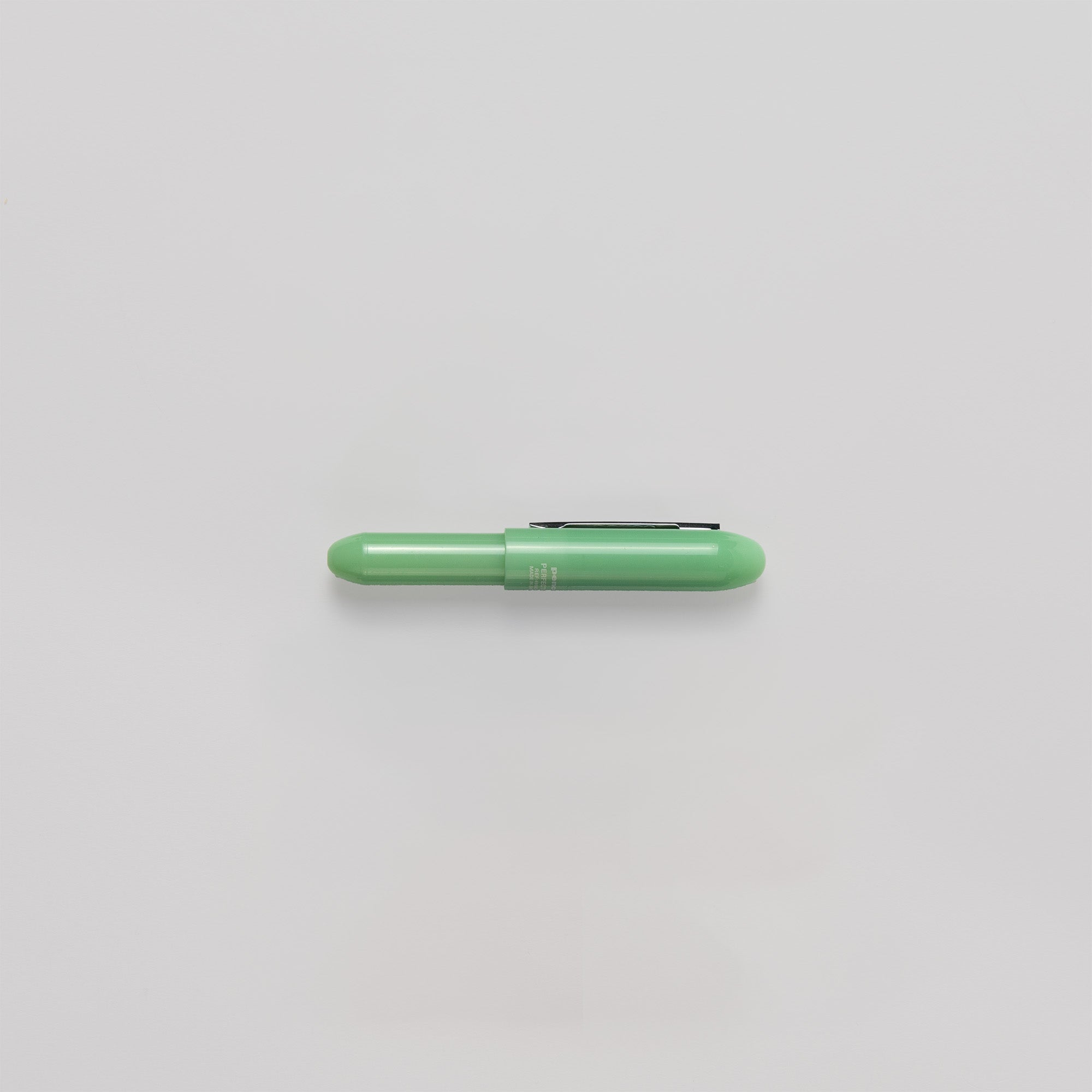 Ein kleiner, grüner Bullet-Kugelschreiber von Penco mit abgerundeter Kappe und Clip liegt horizontal auf einem schlichten weißen Hintergrund. Dieser Stift ist ein Beweis für feine Handwerkskunst aus Japan und sorgt für Präzision bei jedem Strich.