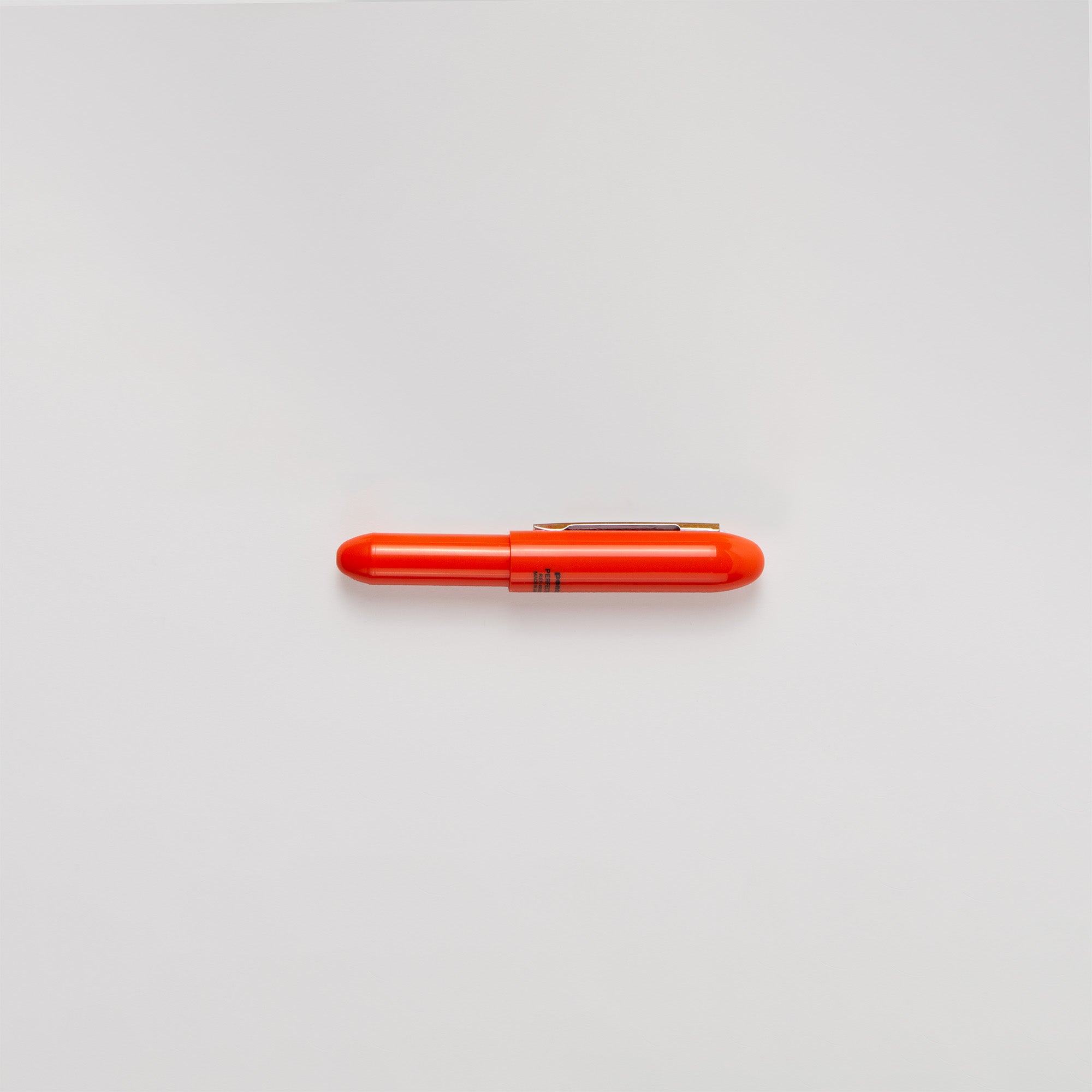 Ein kleiner, leuchtend orangefarbener Bullet-Kugelschreiber von Penco, hergestellt in Japan, ist auf einem schlichten weißen Hintergrund zentriert. Der Stift hat eine glatte zylindrische Form mit einer abgerundeten Spitze und einem Metallclip an der Seite.