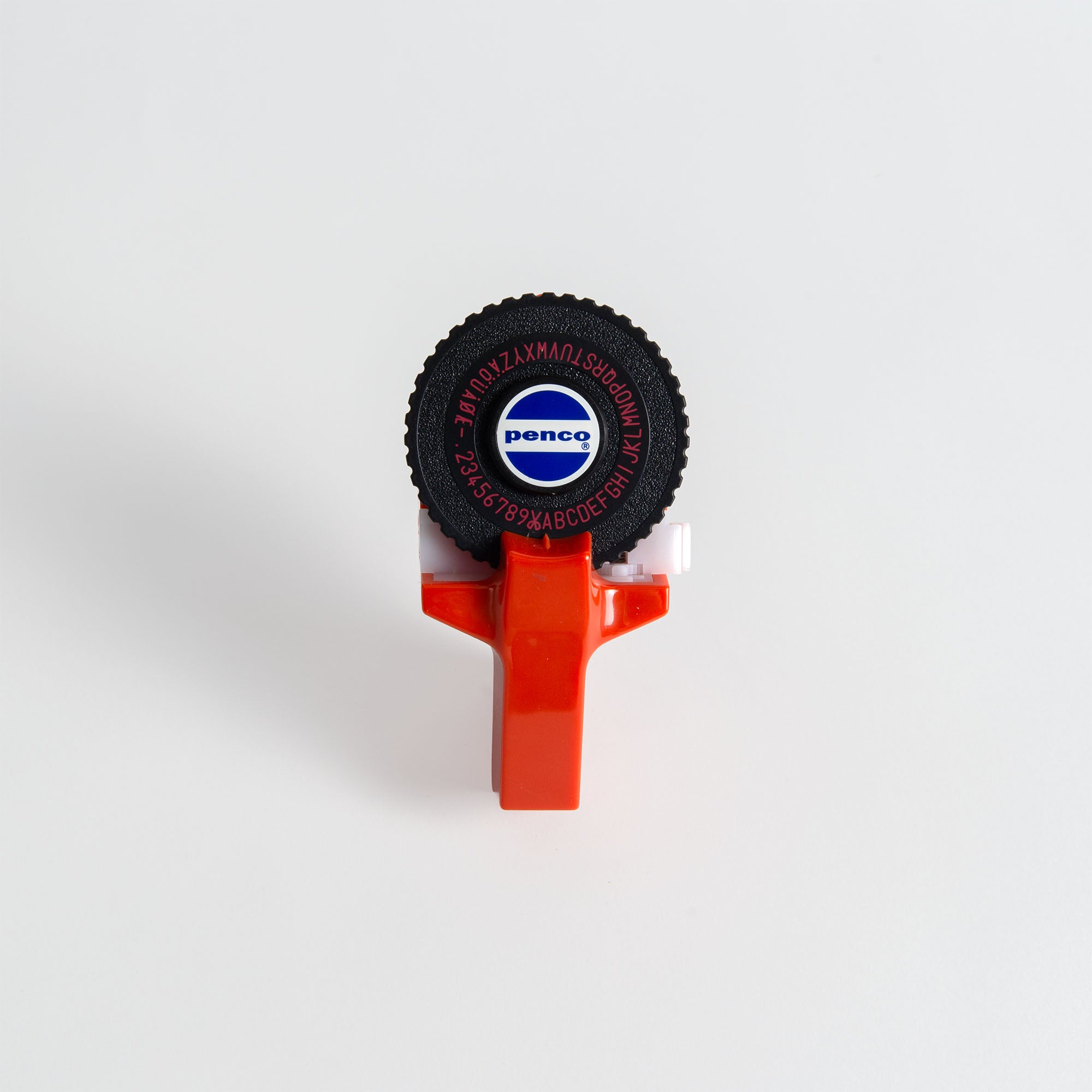 Ein roter Penco Tape Writer von Penco mit einem schwarzen runden Rad mit weißen Buchstaben und Zahlen ruht auf einer schlichten weißen Oberfläche. Der Markenname Penco erscheint in der Mitte dieses alten Etikettierers.
