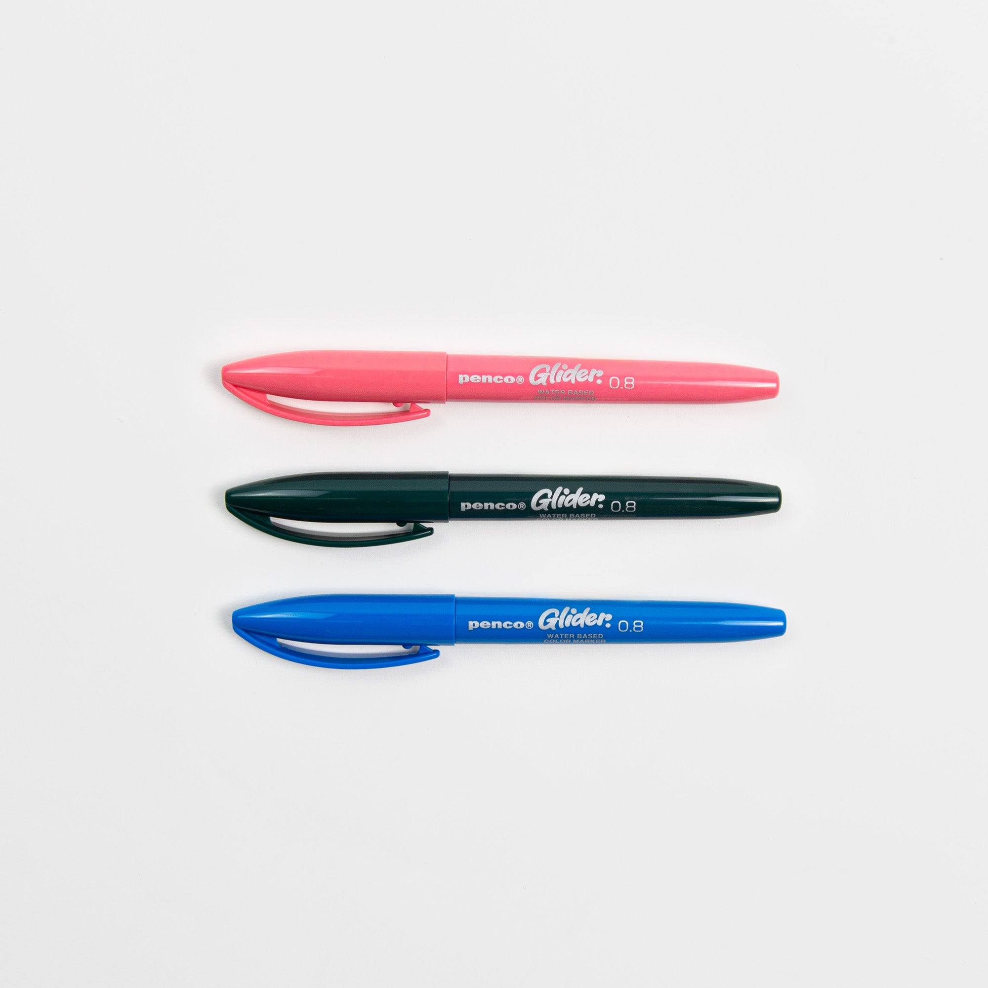 Drei Glider Colour Pens von Penco mit Kappe - rosa, schwarz und blau - liegen parallel auf einer weißen Oberfläche. Jeder Stift trägt das Penco-Etikett und verwendet Tinte auf Wasserbasis für flüssiges Schreiben.