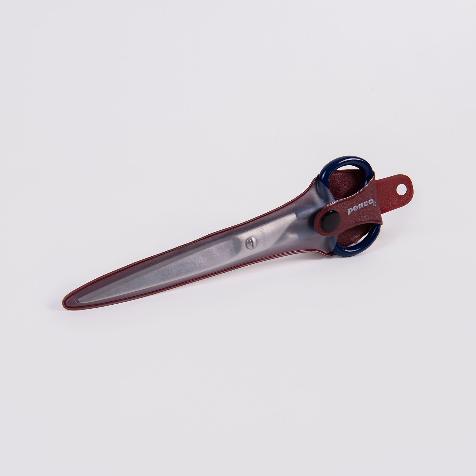 Die Penco Edelstahl Schere - L mit dunkelblauen Griffen ist in einer transparenten PVC-Scheide mit einer roten Lederschlaufe an der Oberseite untergebracht. Die Scheide bedeckt die Klinge vollständig. Beide sind vor einem schlichten weißen Hintergrund abgebildet.