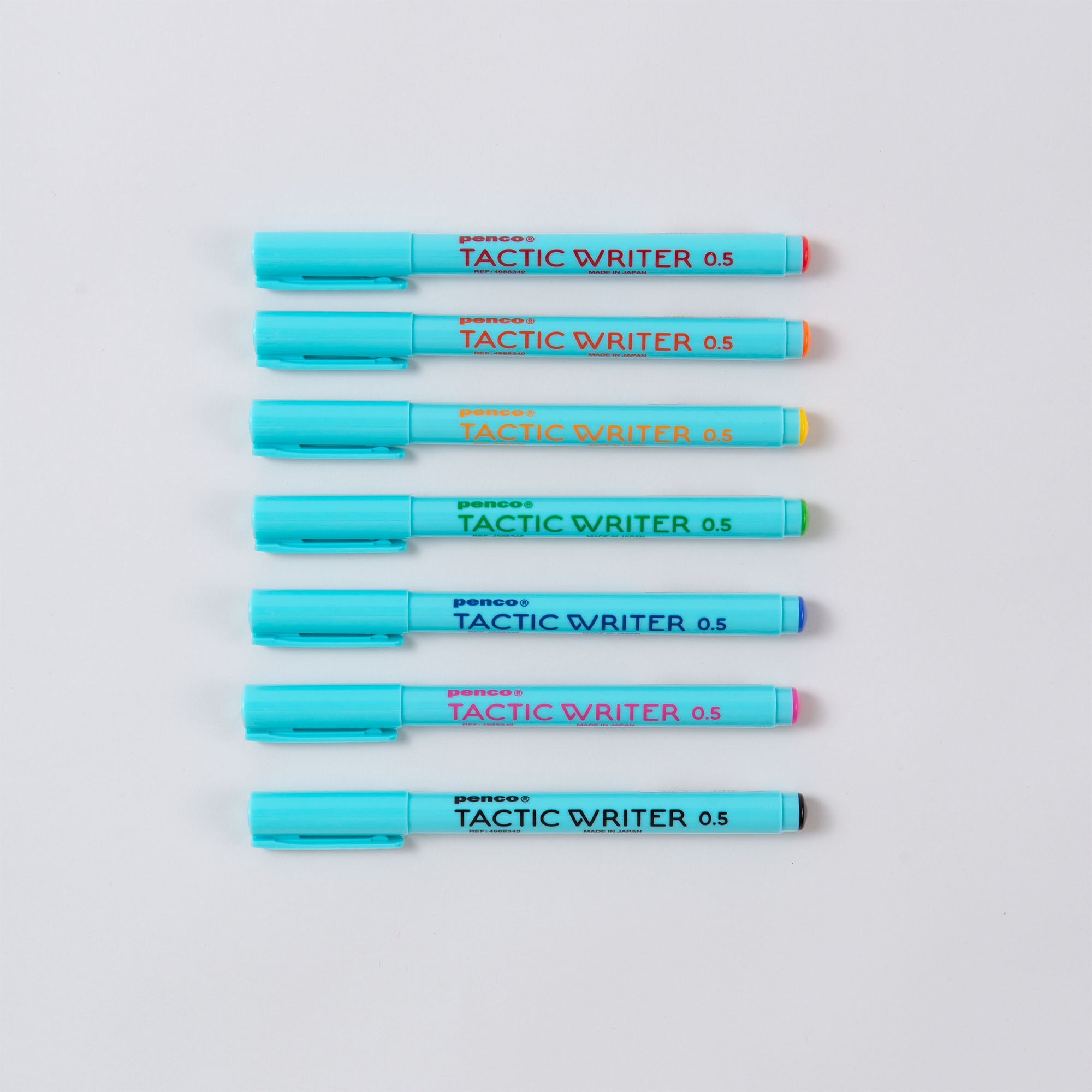 Sieben blaue Marker aus dem Penco „Tactic Writer Set – 7 Farben zum Schreiben, Markieren, Zeichnen“ sind horizontal auf einer weißen Fläche angeordnet. Jeder hat eine farbige Spitze: Rot, Orange, Gelb, Grün, Blau, Lila und Rosa. Sie verfügen über eine wasserbasierte Tinte, die sich perfekt für schöne Schriftkunst eignet.