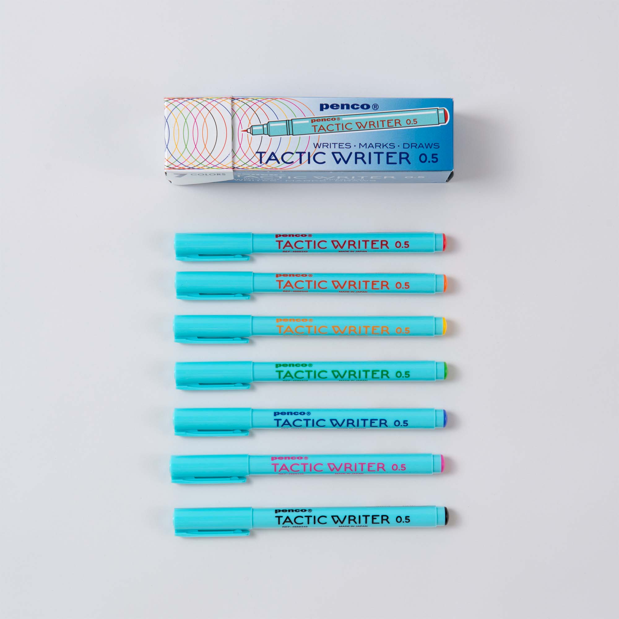 Über einer Schachtel mit der Aufschrift „Tactic Writer 0.5“ ist ein Stift zu sehen. Darunter sind ordentlich sieben Penco-Stifte in Hellblau, Orange, Rosa, Grün, Rot, Gelb und Lila angeordnet. Jeder Stift verfügt über Schönschrift-Funktionen mit wasserbasierter Tinte und gehört zum Tactic Writer Set von Penco – 7 Farben zum Schreiben, Markieren, Zeichnen.