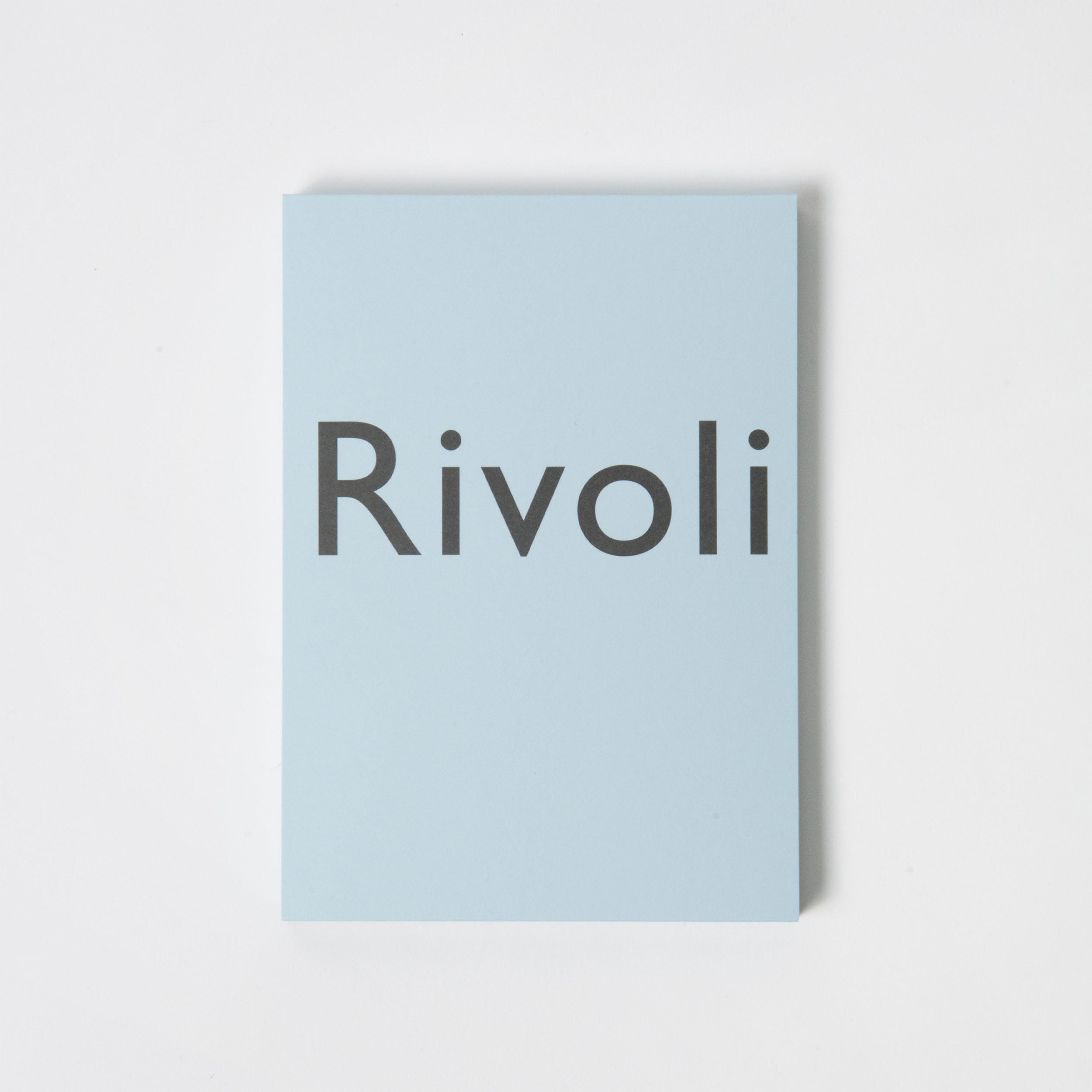 Eine hochwertige hellblaue rechteckige Karte, die Briefpapier ähnelt, trägt in großen, fettgedruckten schwarzen Buchstaben das Wort „Rivoli“. Das elegante Design von Carta Pura auf dem Skizzen- und Schreibblock Rivoli hellblau wird durch einen makellosen weißen Hintergrund hervorgehoben.