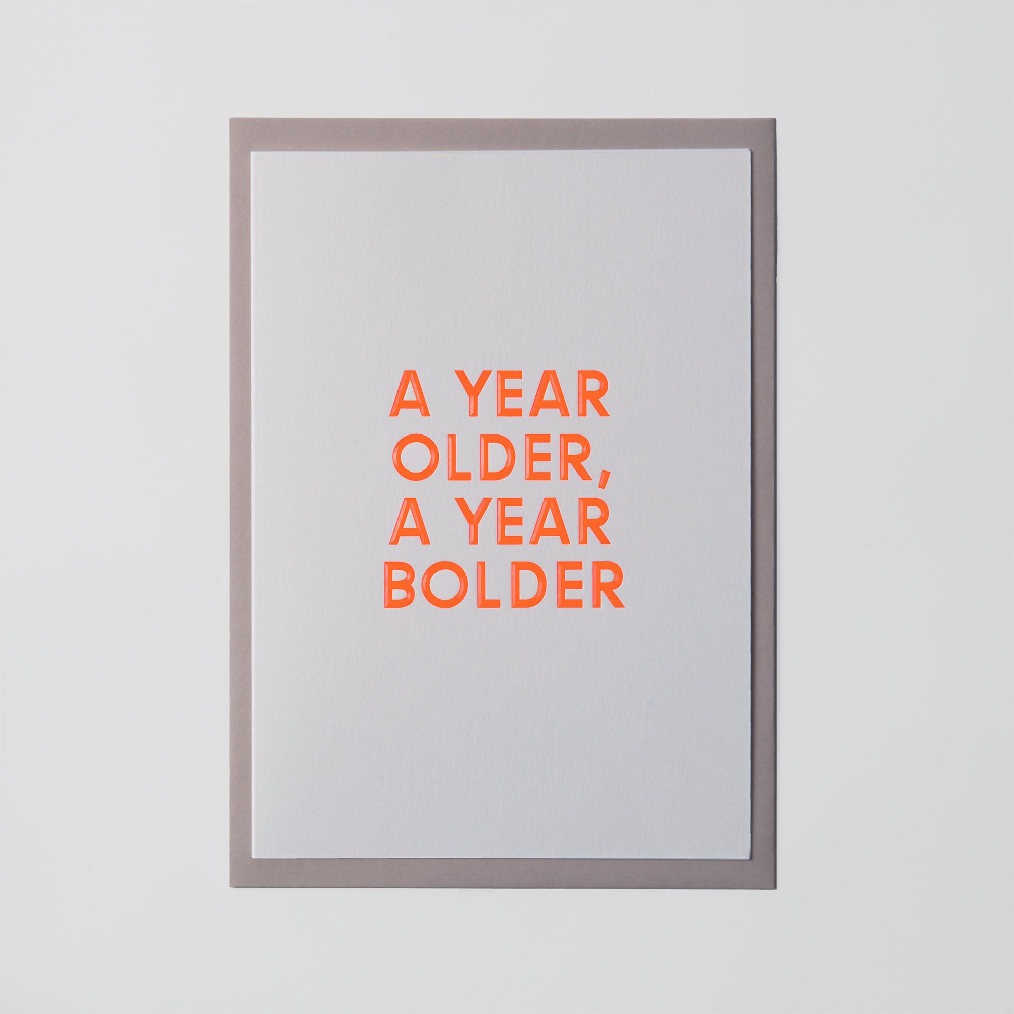 Das Bild zeigt die Geburtstagskarte „AYOAYB“ von paperlux.store mit der Aufschrift „A YEAR OLDER, A YEAR BOLDER“ in kräftigem Orange auf weißem Hintergrund, umrahmt von Grau. Das Design wird durch eine elegante Heißfolienprägung für ein auffälliges Finish aufgewertet.