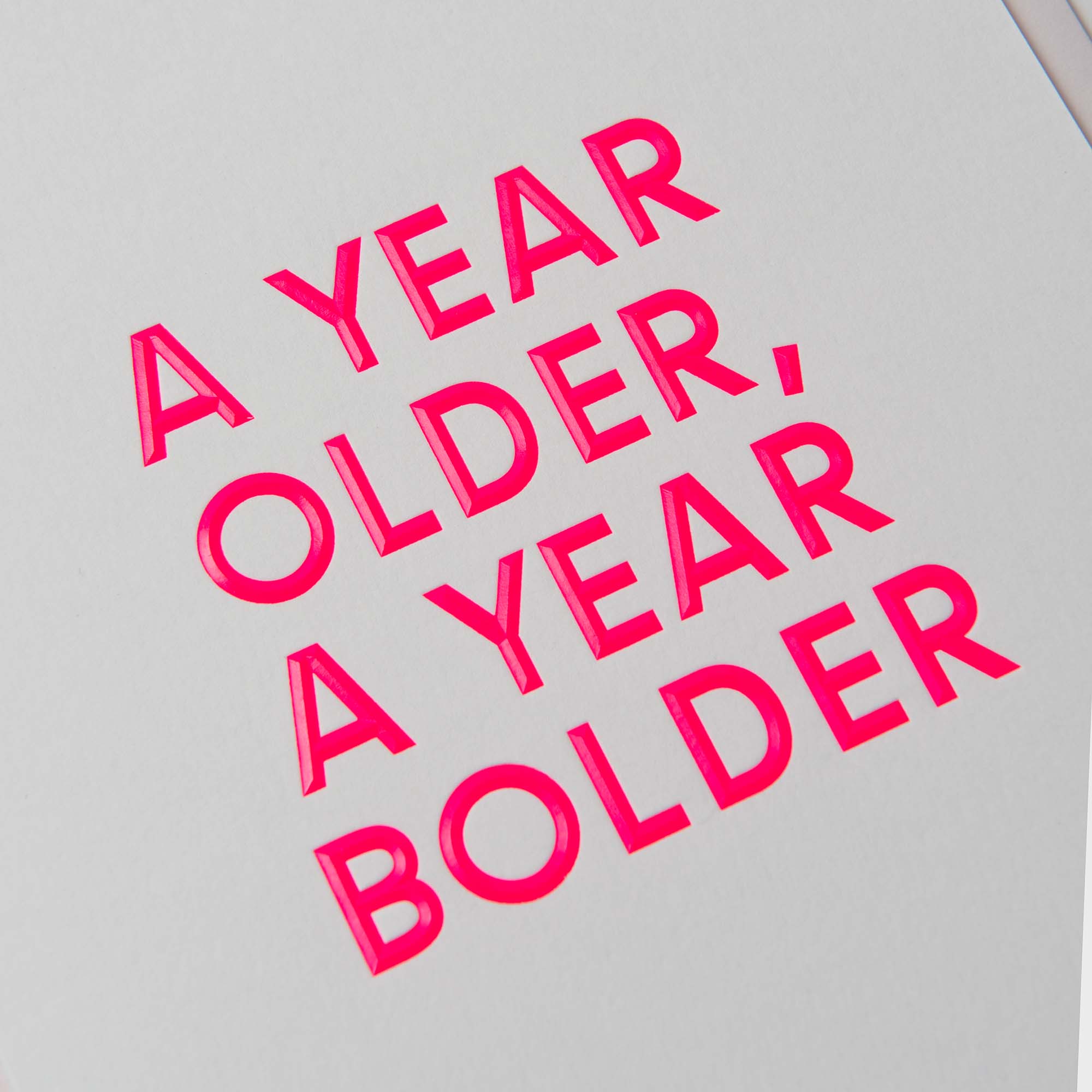 Die Geburtstagskarte „AYOAYB“ von paperlux.store zeigt den fettgedruckten rosa Text „A YEAR OLDER, A YEAR BOLDER“ auf weißem Hintergrund mit eleganter Heißfolienprägung.