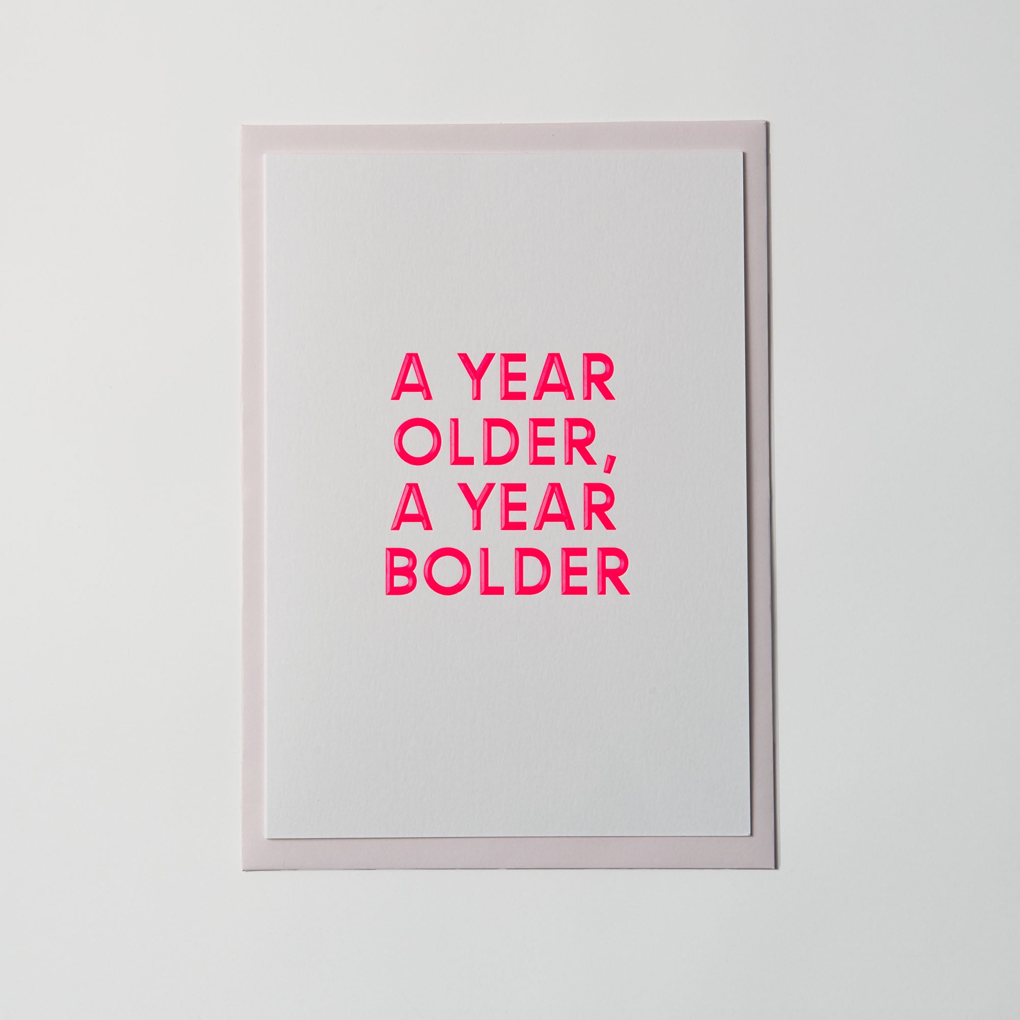 Die Geburtstagskarte „AYOAYB“ von paperlux.store zeigt „A YEAR OLDER, A YEAR BOLDER“ in kräftigem Pink auf weißem Feinstpapier, aufgesetzt auf ein elegantes Hellgrau für einen modernen Touch.