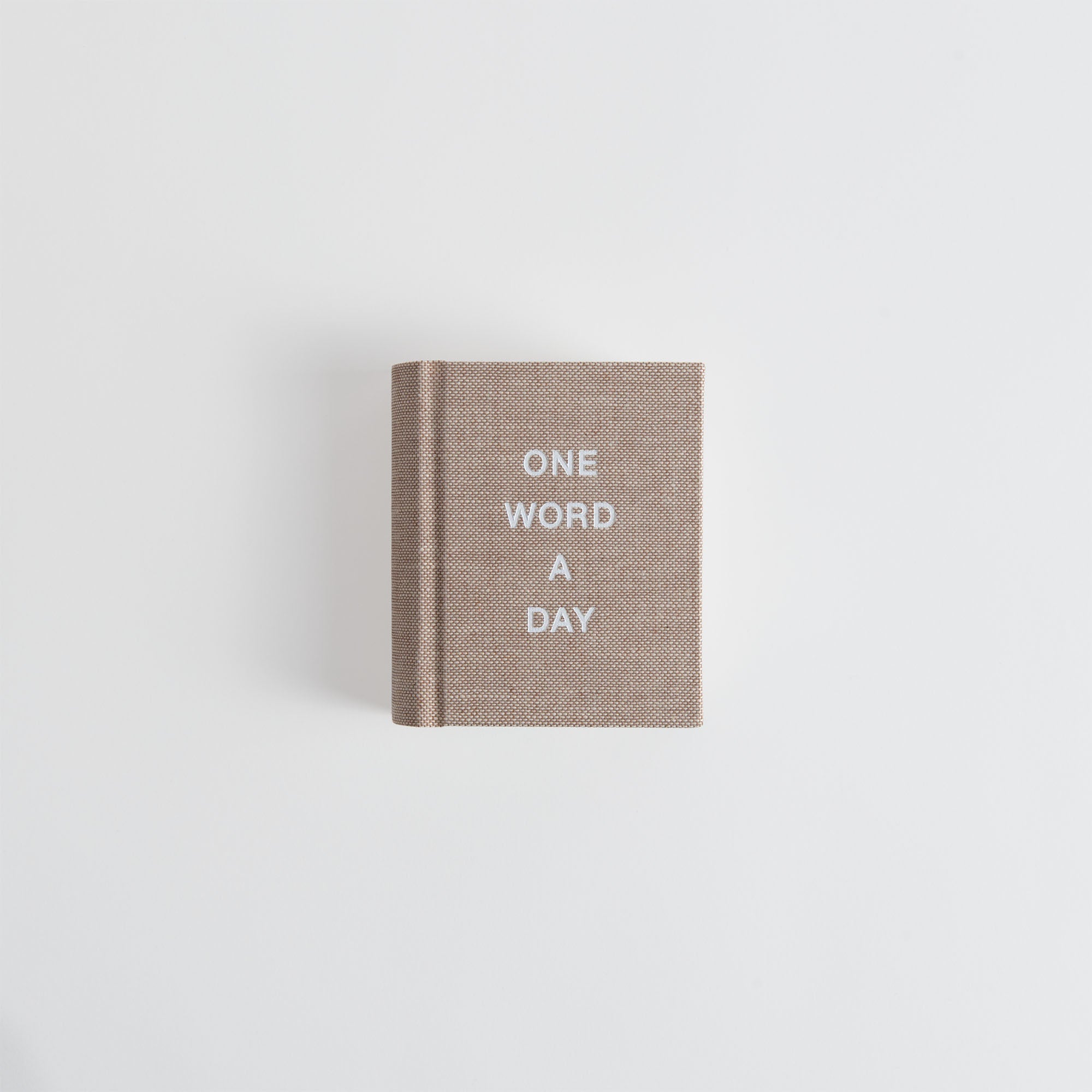 Das Buch OWAD Hygge Collection von paperlux.store, ein kleiner brauner Band mit "ONE WORD A DAY" in weißen Großbuchstaben, steht mittig auf einem schlichten weißen Hintergrund.