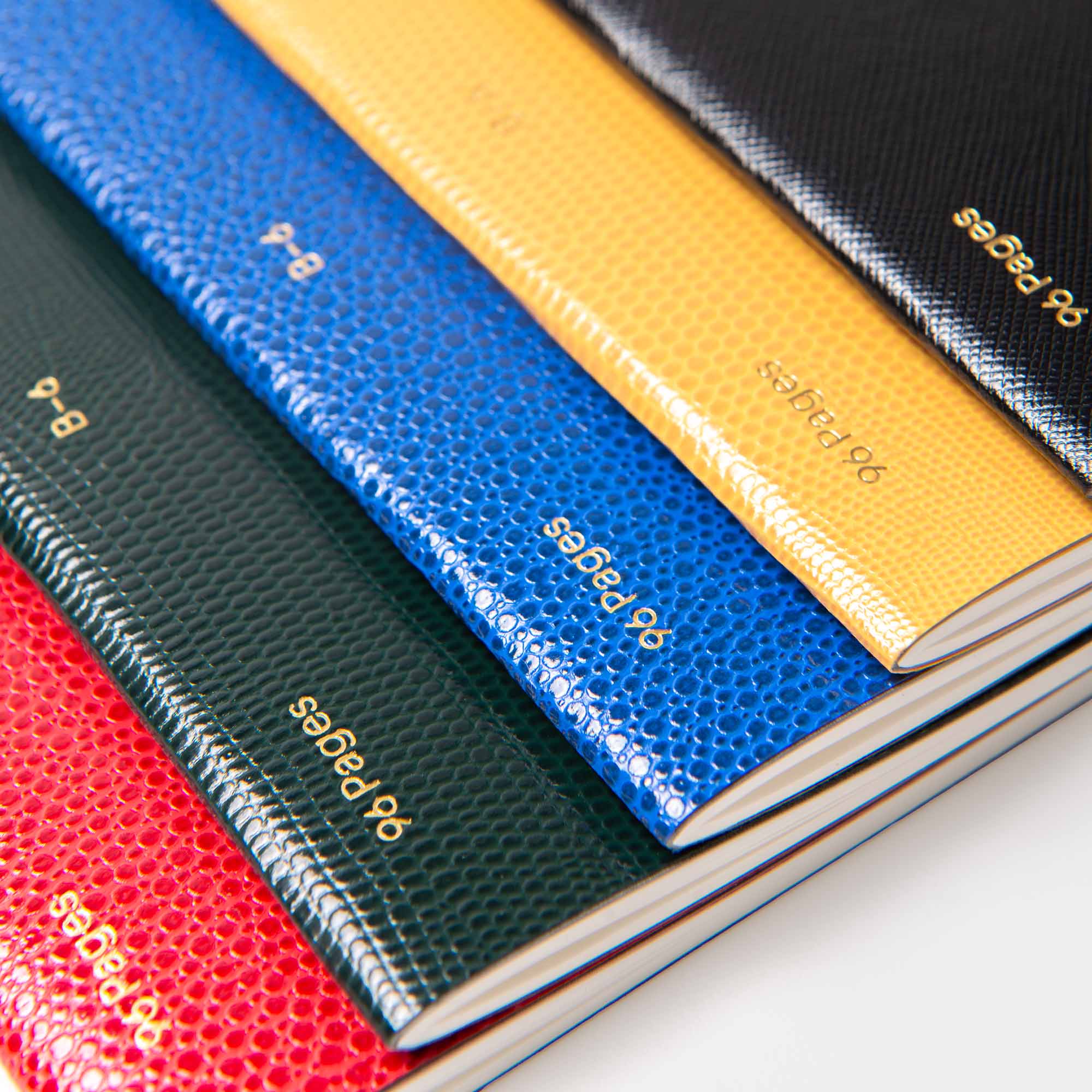 Fünf B96 Mellow Yellow Softcover Notizbücher von paperlux.store sind diagonal gestapelt. Jedes hat eine Goldprägung "90 Seiten" auf dem Rücken und ist in schlanker, sauber ausgerichteter Notizbuch Lederoptik gestaltet.