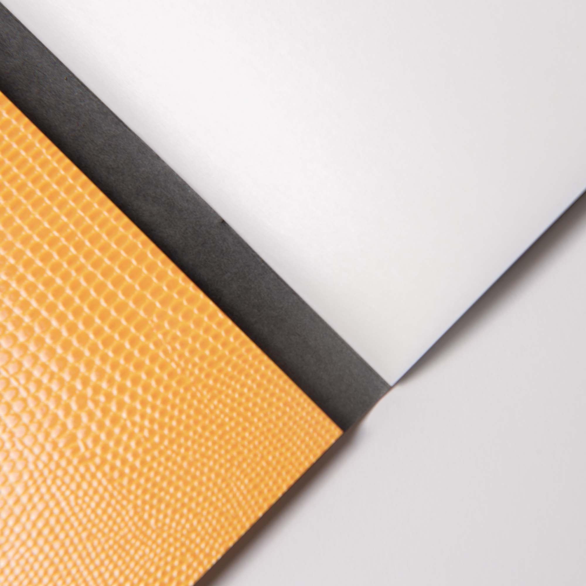 Eine Nahaufnahme des B96 Mellow Yellow Notizbuchs von paperlux.store zeigt ein strukturiertes gelbes Softcover, einen schwarzen Buchrücken und weiße Seiten, die diagonal auf einer hellen Oberfläche liegen.
