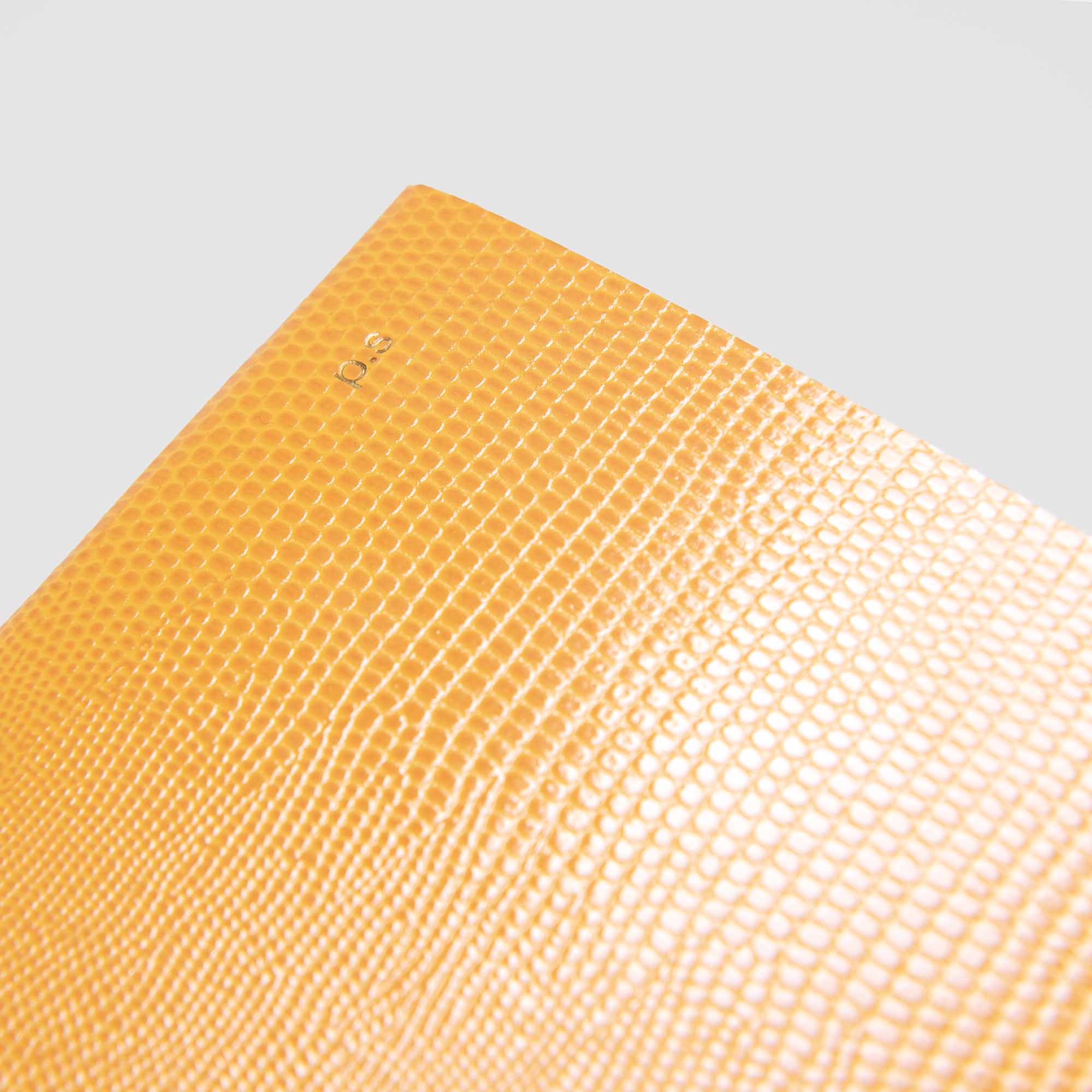 Nahaufnahme des Softcovers B96 Mellow Yellow von paperlux.store mit einer orangefarbenen Oberfläche in Lederoptik und einer kleinen Goldprägung "03" oben links auf einem einfarbigen Hintergrund aus hellem Wolkenpapier.