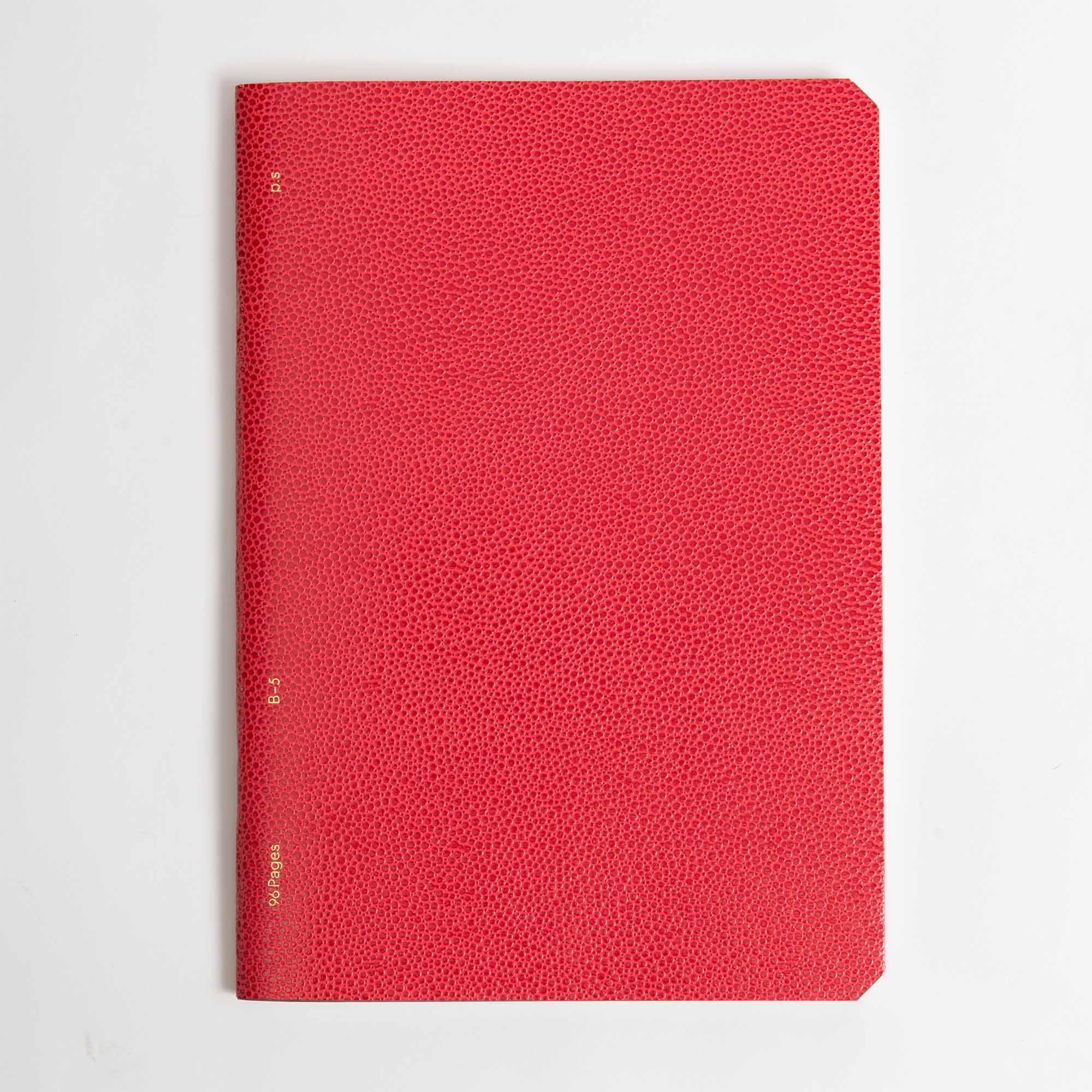 Ein geschlossenes, rot strukturiertes paperlux.store Softcover Notizbuch (B96 Red Lipstick) mit abgerundeten Ecken ruht auf einem weißen Hintergrund. Ein kleiner goldener Text erscheint vertikal am linken Rand und erinnert an ein schickes Red Lipstick-Accessoire.
