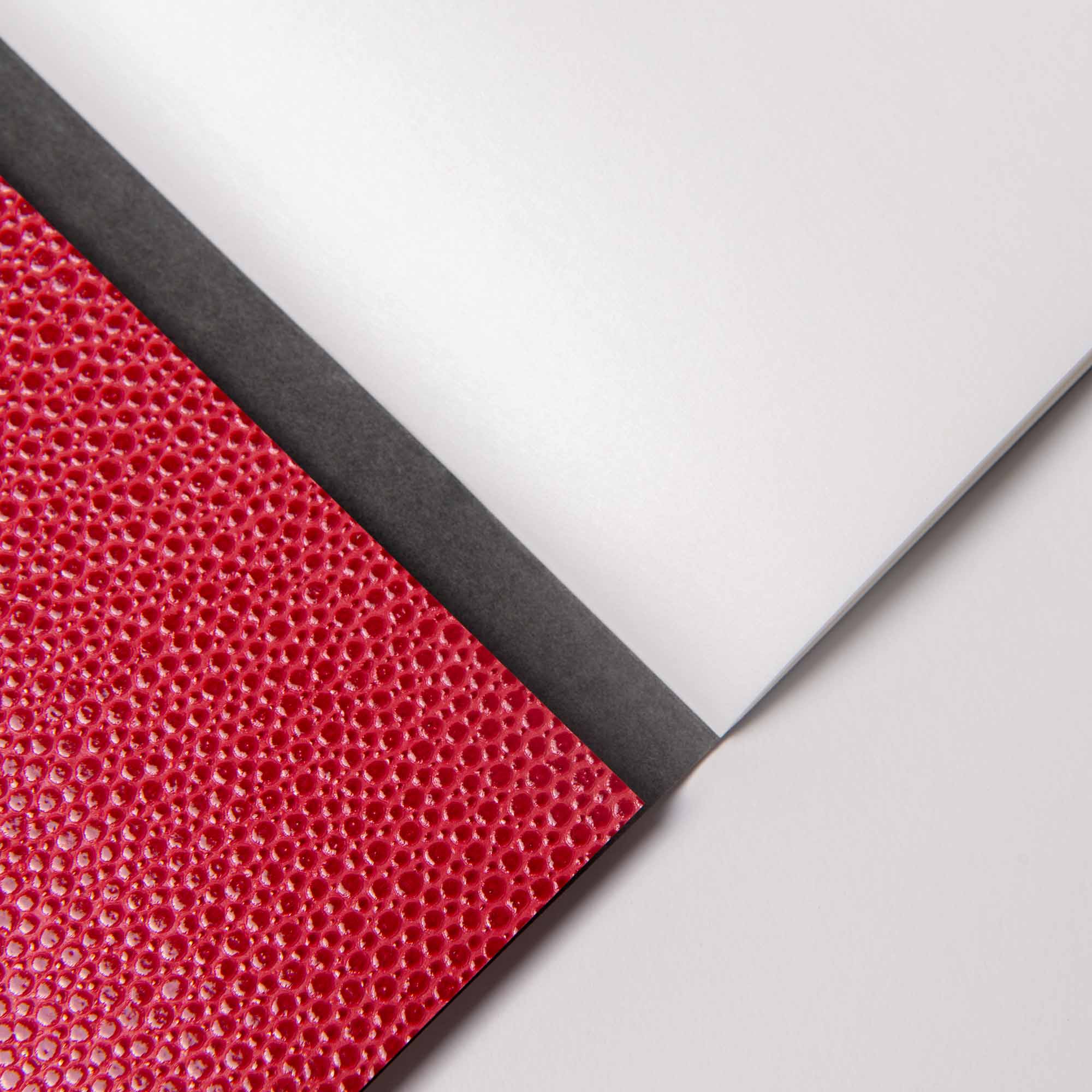 Nahaufnahme des paperlux.store B96 Red Lipstick Softcover-Notizbuchs mit strukturiertem rotem Einband, schwarzem Rücken und leeren weißen Cloud Paper-Seiten auf einer hellen Oberfläche.