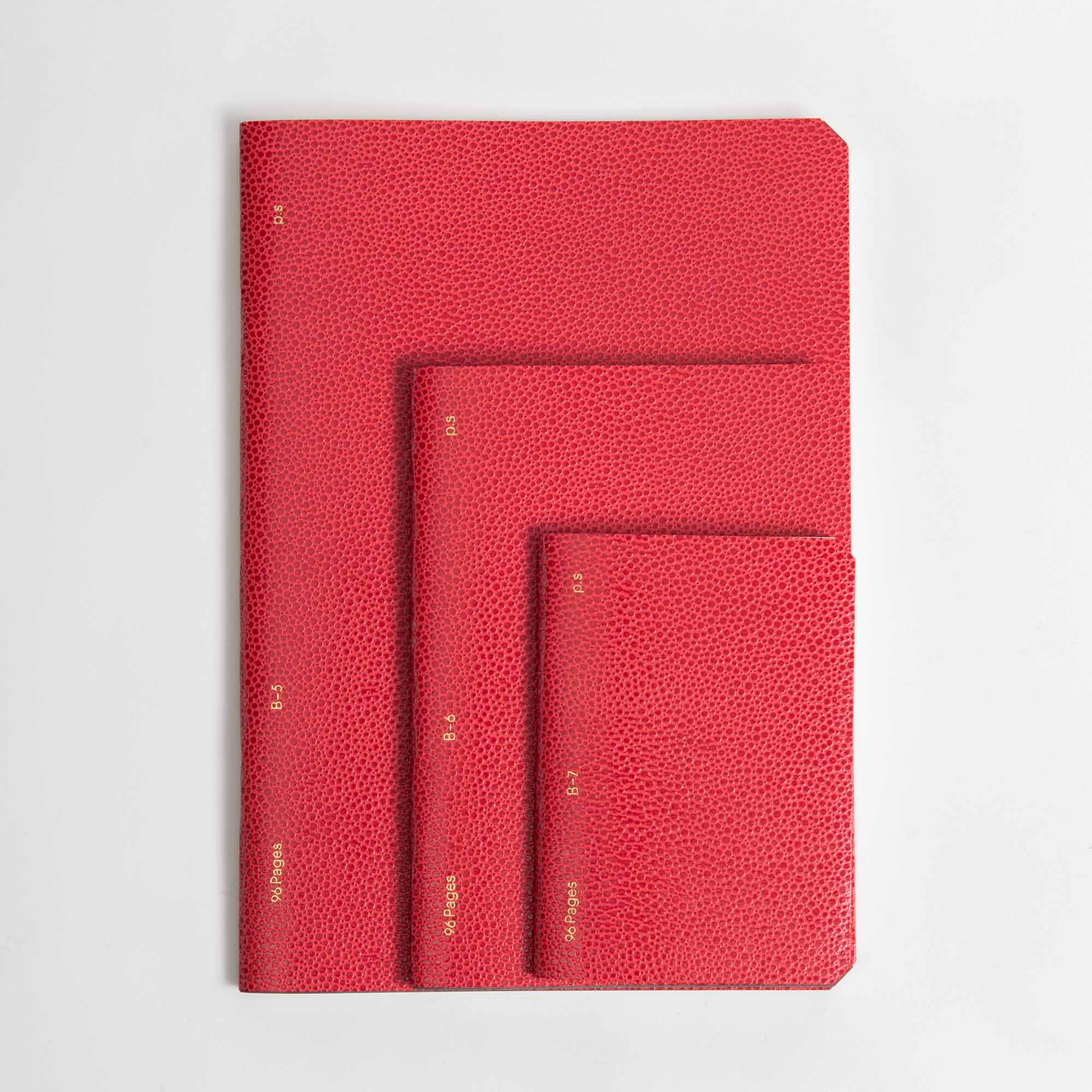 Drei B96 Red Lipstick Softcover Notizbücher von paperlux.store, jedes in einer anderen Größe und mit den Goldfolien-Initialen N/S, N/M und N/L auf dem Buchrücken, sind auf einer weißen Fläche gestapelt.