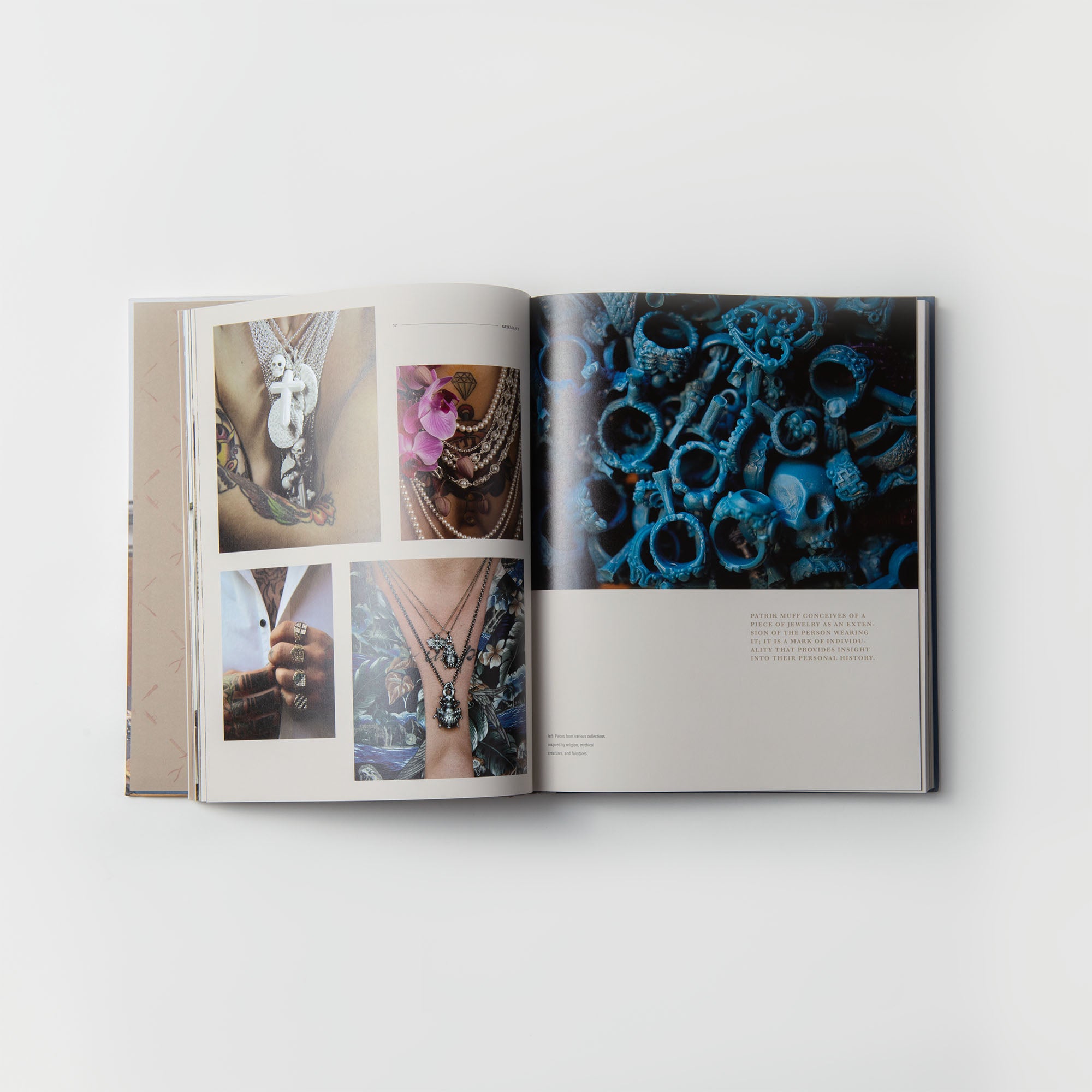 „Das Handwerk und die Macher“ vom Gestalten Verlag ist auf einer weißen Fläche aufgeschlagen und hebt erlesenen Schmuck hervor. Auf der linken Seite sind atemberaubende Fotos von Halsketten zu sehen, während auf der rechten Seite blau getönte Ringe und ein Textblock zur Würdigung der Kunstfertigkeit der Buchbinderei zu sehen sind.