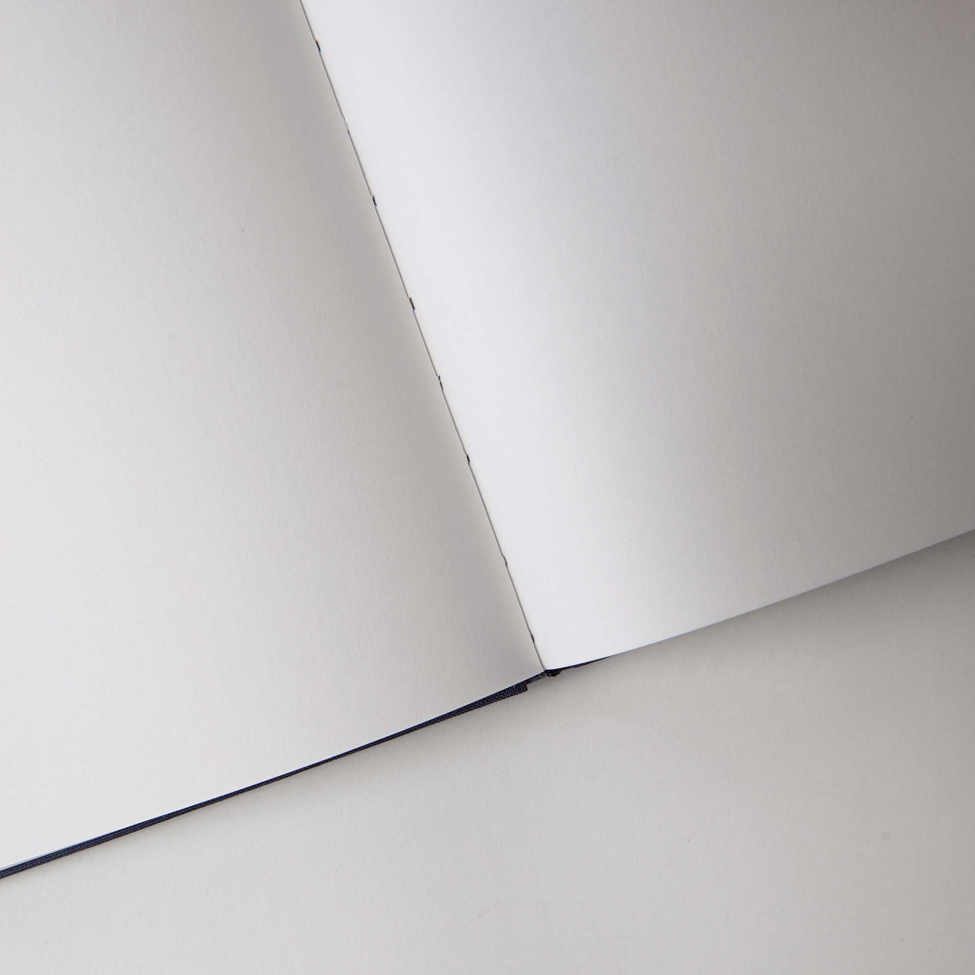 Ein Notanizer Notizbuch A5 von paperlux.store mit makellosen weißen Seiten aus Feinstpapier liegt offen auf einer hellgrauen Oberfläche. Der leicht gebogene Rücken zeigt die leeren Seiten und lädt zu Kreativität und einem „You do You“-Geist für persönlichen Ausdruck ein.