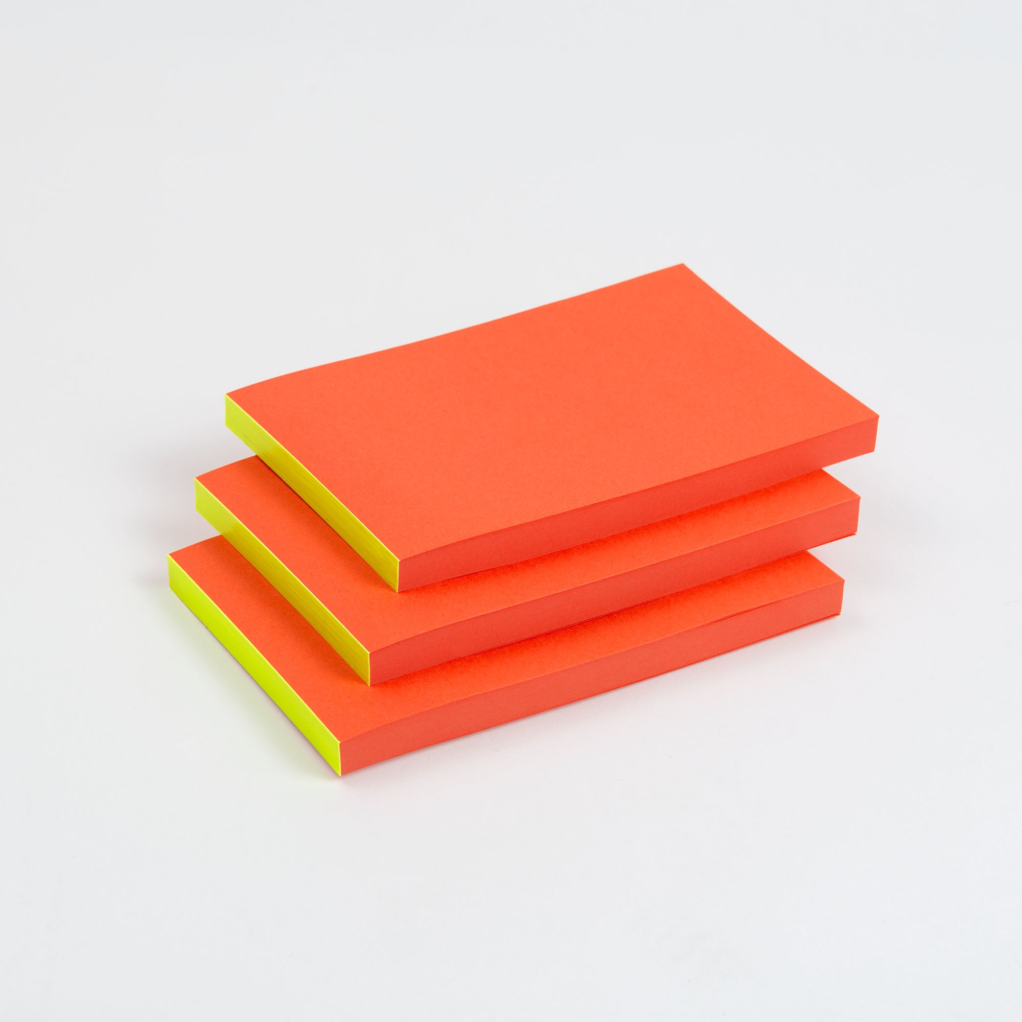 Drei gestapelte Abreissblöcke Neon von paperlux mit orangefarbenen Oberseiten und gelben Seiten aus hochwertigen Feinstpapier-Resten im DIN lang Format. Ideal zum Organisieren Ihrer Besten Reste auf jedem Schreibtisch.