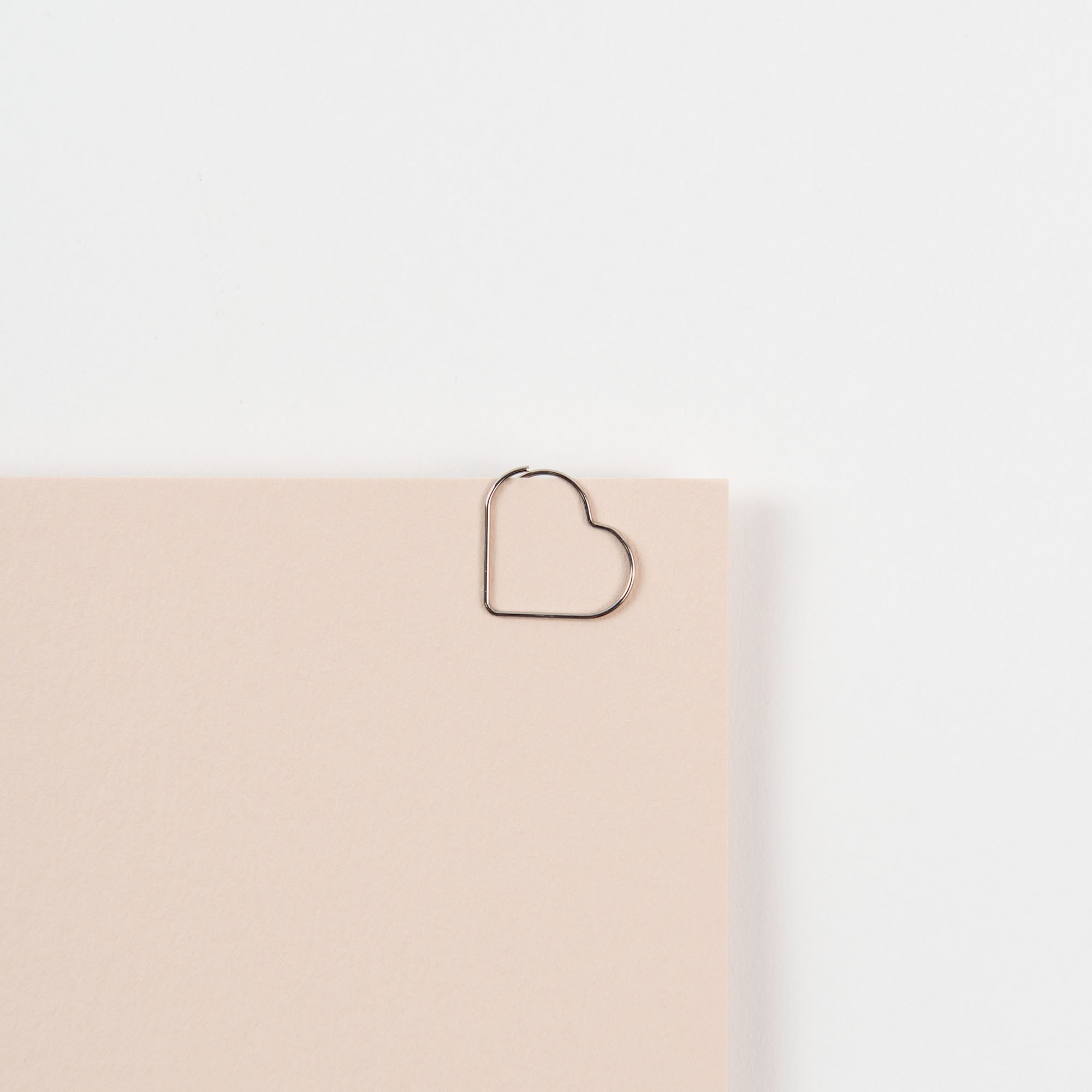 Ein beiges Blatt Papier, ähnlich einer Notiz oder einem Liebesbrief, wird mit den D-Clips Nano: Herzen für Alle von Midori vor einem makellos weißen Hintergrund befestigt.