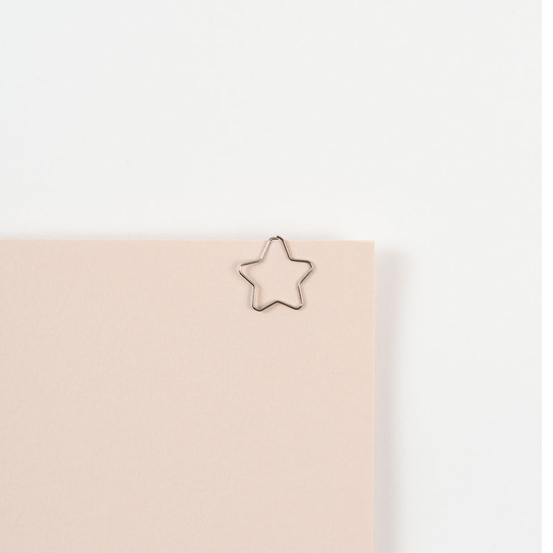 Ein beiges Blatt Papier mit einer sternförmigen Büroklammer vom Typ Midori D-Clips Nano: Sterne am oberen Rand. Die Klammer zeigt ein Tiermotiv und ist auf weißem Hintergrund angebracht.