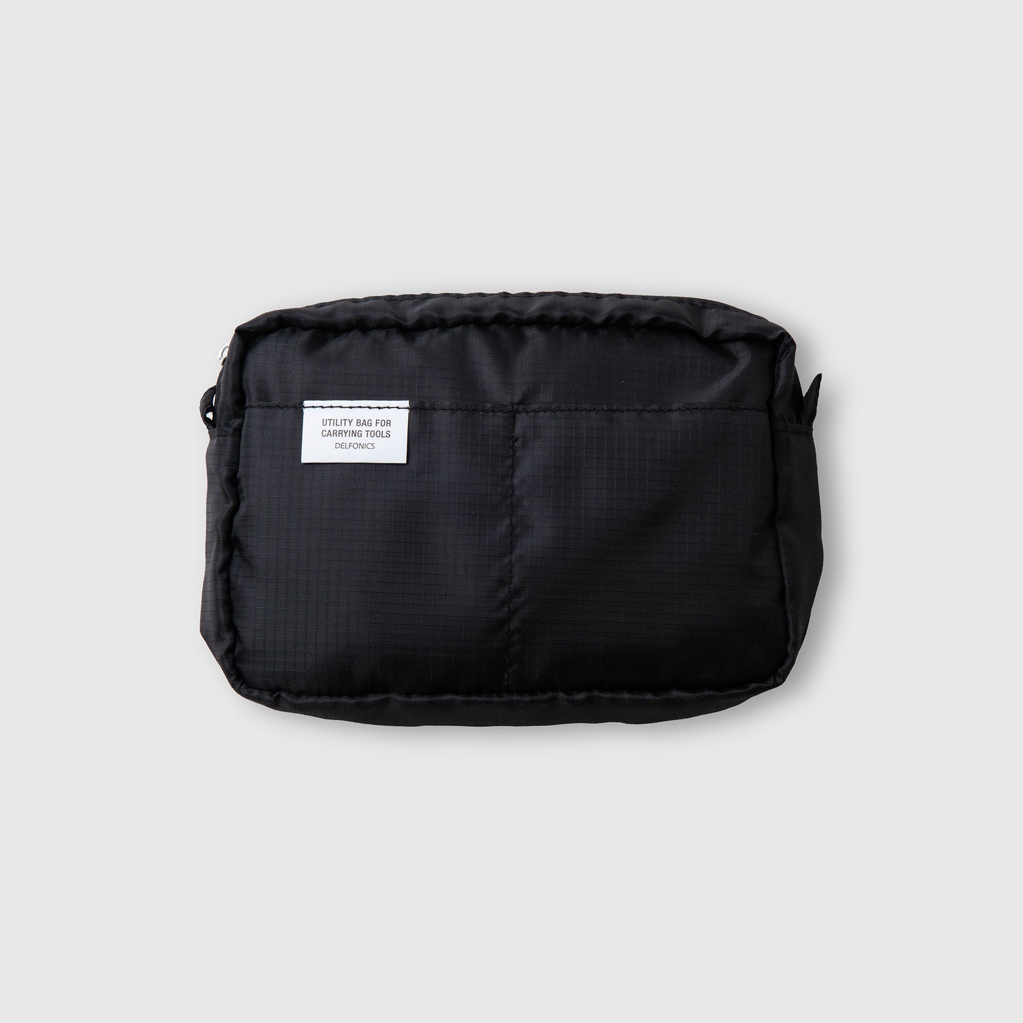 Die Delfonics Inner Carrying Case AIR S von Delfonics ist eine kleine, schwarze, rechteckige Tragetasche aus strapazierfähigem Ripstop-Gewebe. Sie verfügt über eine Vordertasche und ein weißes Etikett oben links, das sich von einem schlichten hellgrauen Hintergrund abhebt.
