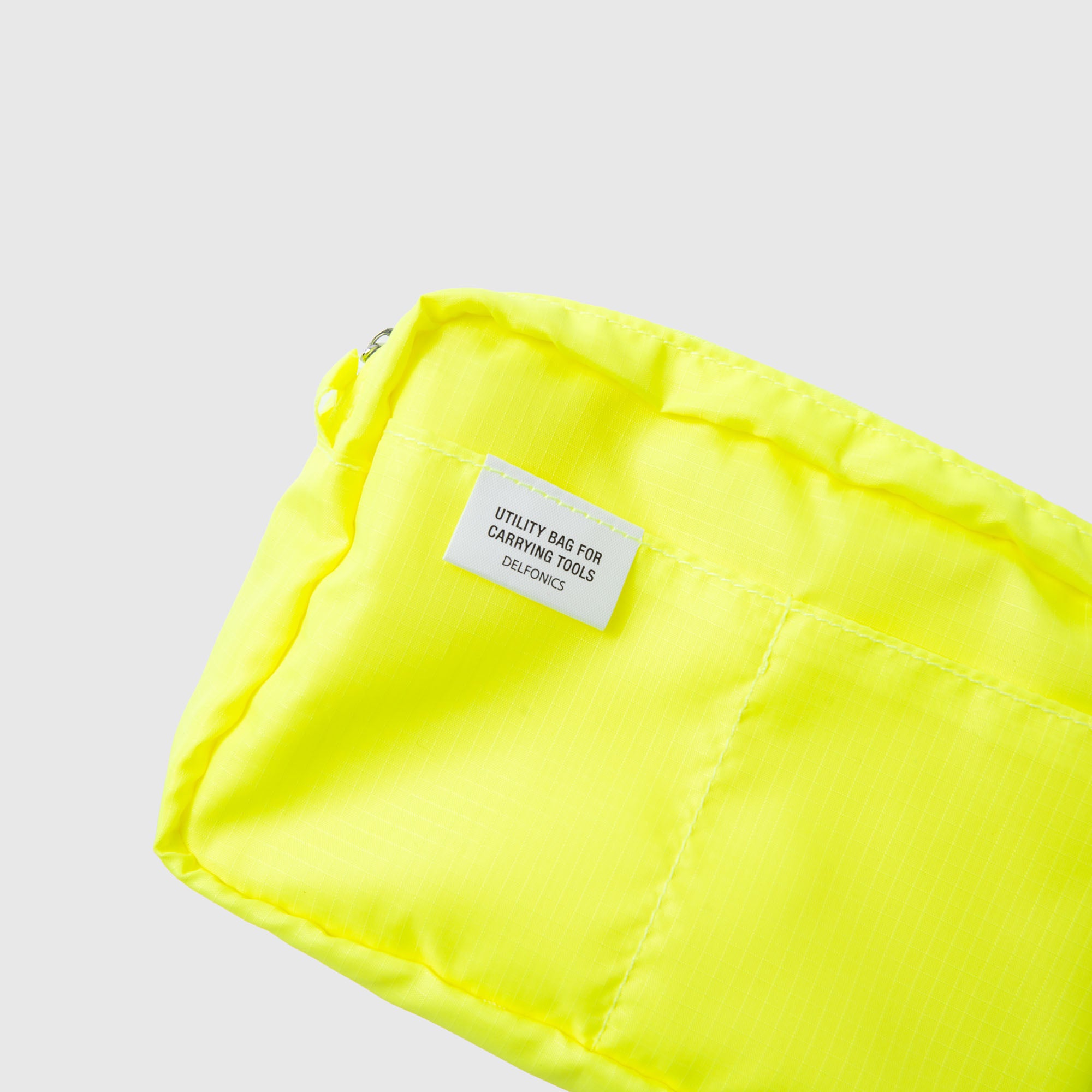 Eine leuchtend gelbe Delfonics-Innentasche „AIR S“ aus strapazierfähigem Ripstop-Gewebe mit einem weißen Etikett, auf dem „UTILITY BAG FOR CARRYING TOOLS DELICIOUS“ steht, ist vor einem schlichten hellen Hintergrund abgebildet.