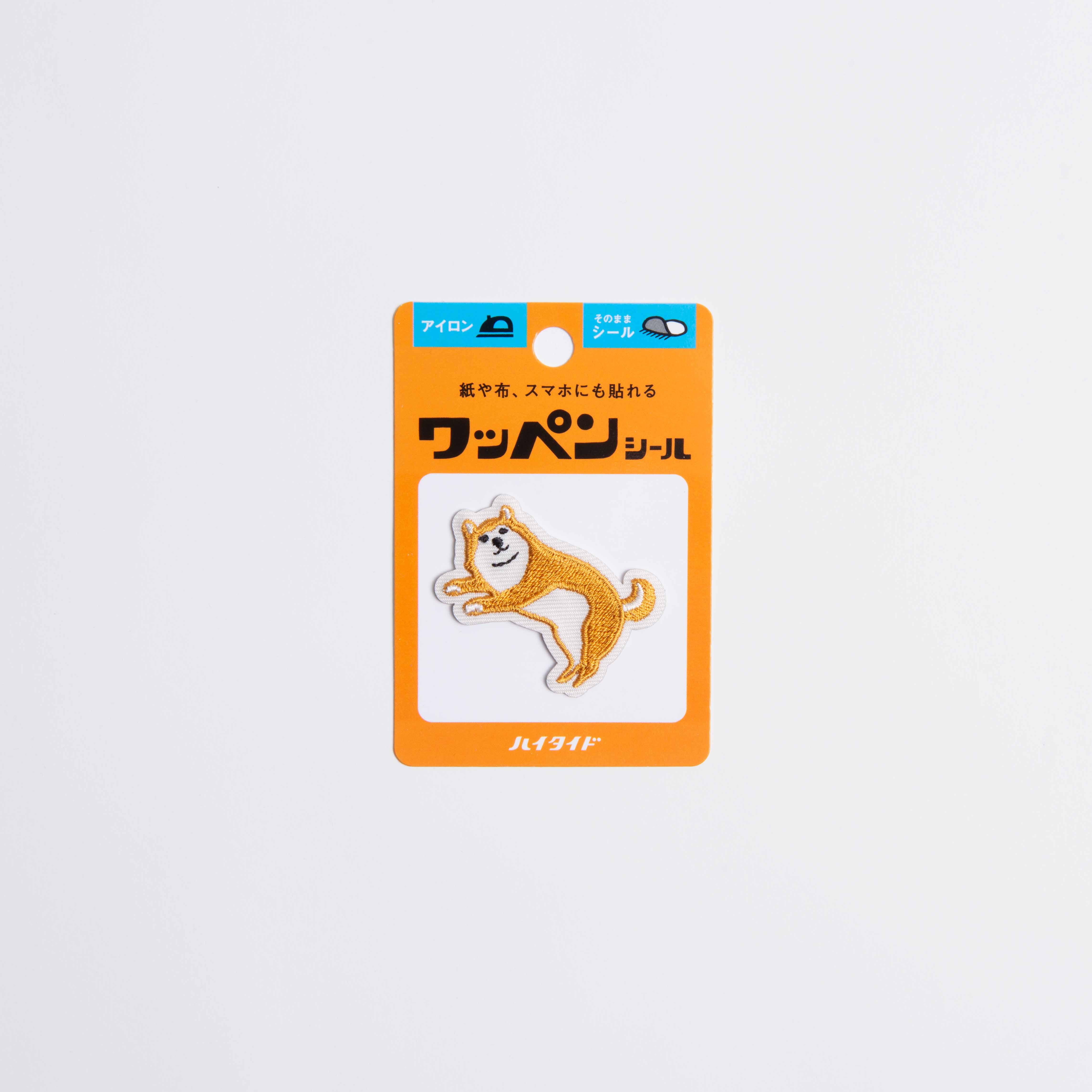 Der Hightide New Retro Patch Sticker von Hightide zeigt einen kleinen gestickten Shiba Inu Hund auf einer orange-weißen Karte mit japanischem Text und einer durchsichtigen Plastikhülle, die an die Showa-Ära erinnert.
