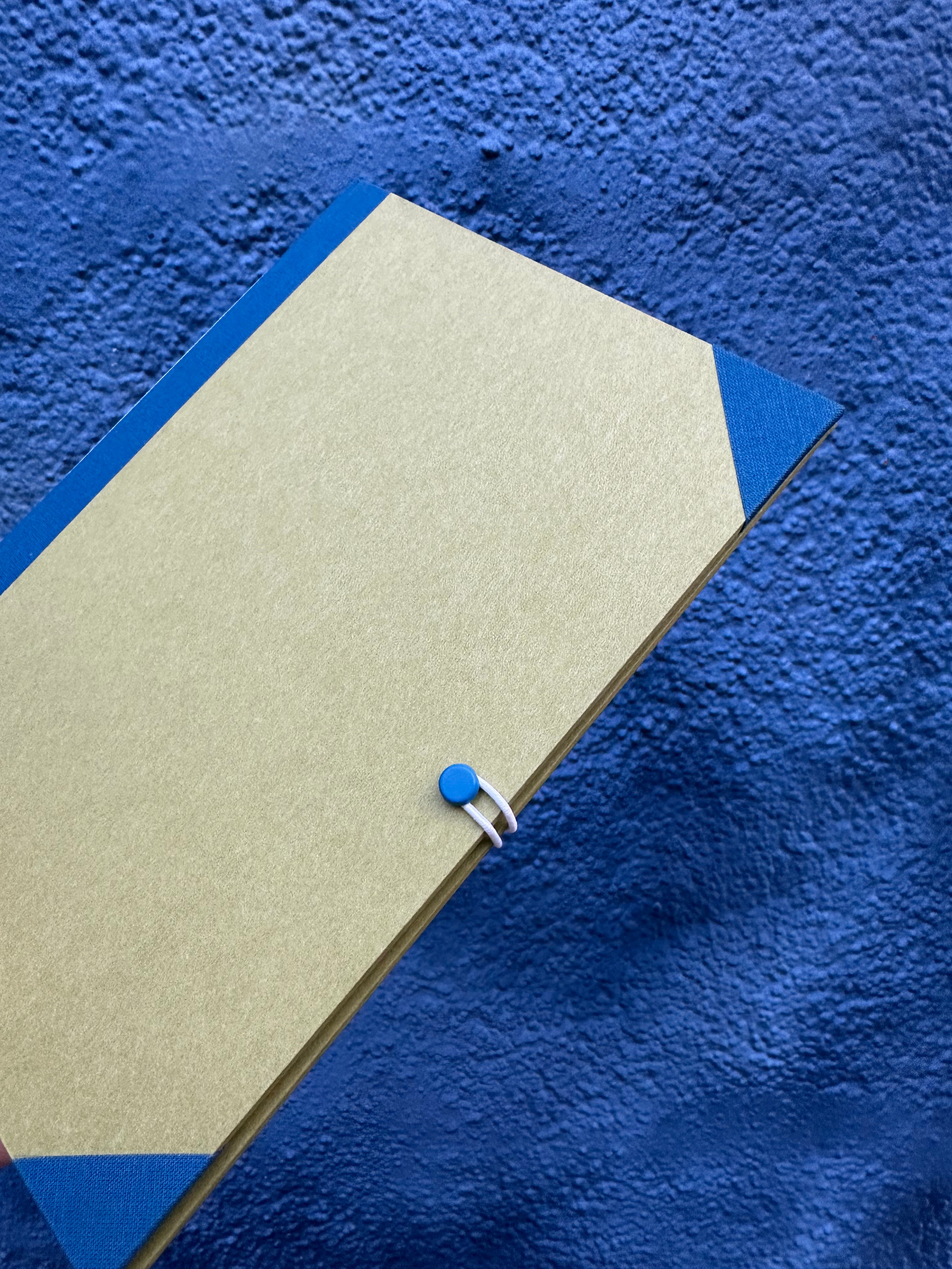Beiges Paperlux-Workshop-Notizbuch Modulares Notizbuch mit blauen Akzenten an den Ecken und einem blauen Knopfverschluss mit weißem Gummiband.