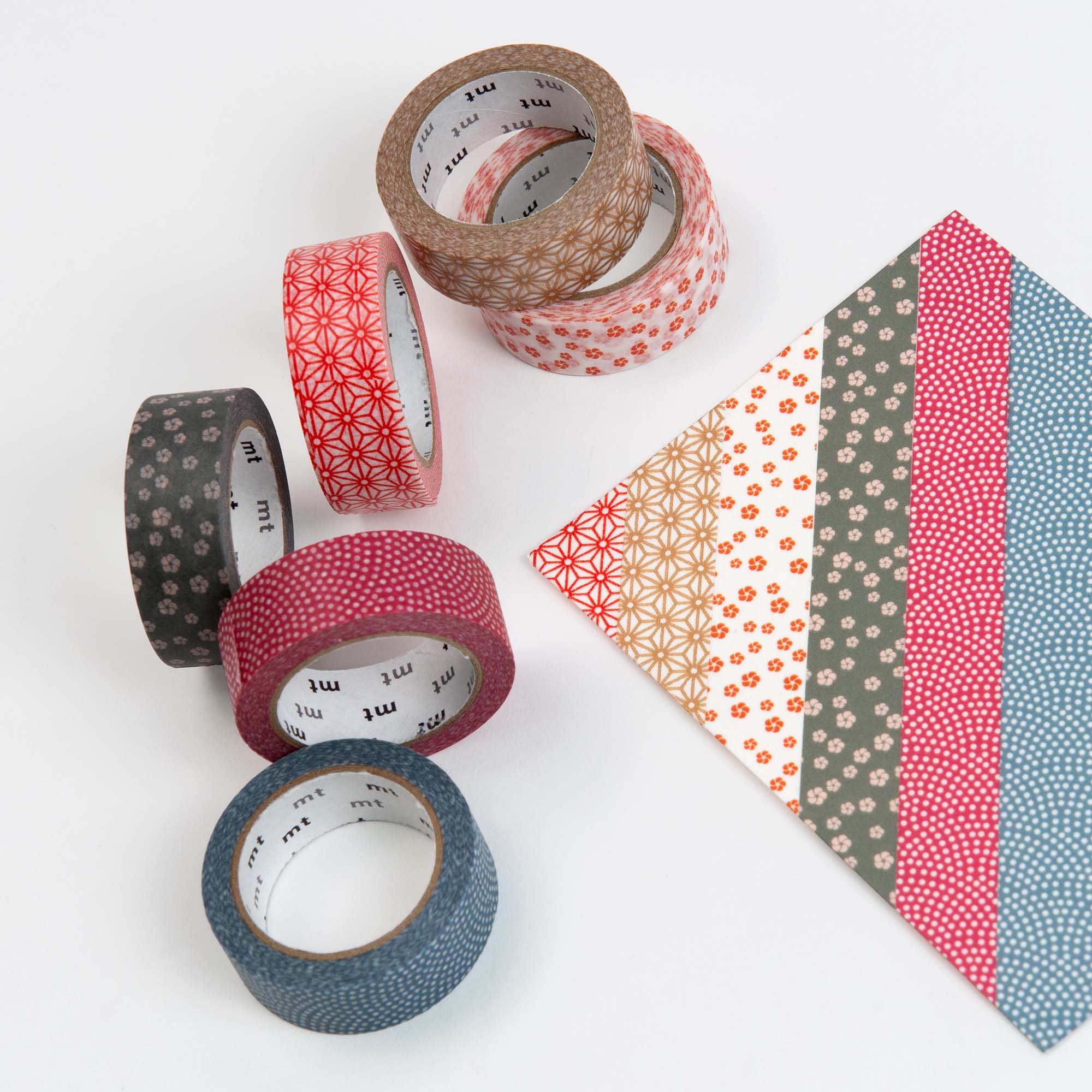 Sechs Rollen Kamoi Kakoshi mt Washi Tape - Wamon 5 Geschenkbox mit japanischen Mustern sind neben einem Papier angeordnet, das mit passenden diagonalen Streifen aus den gleichen Klebebandmustern verziert ist.